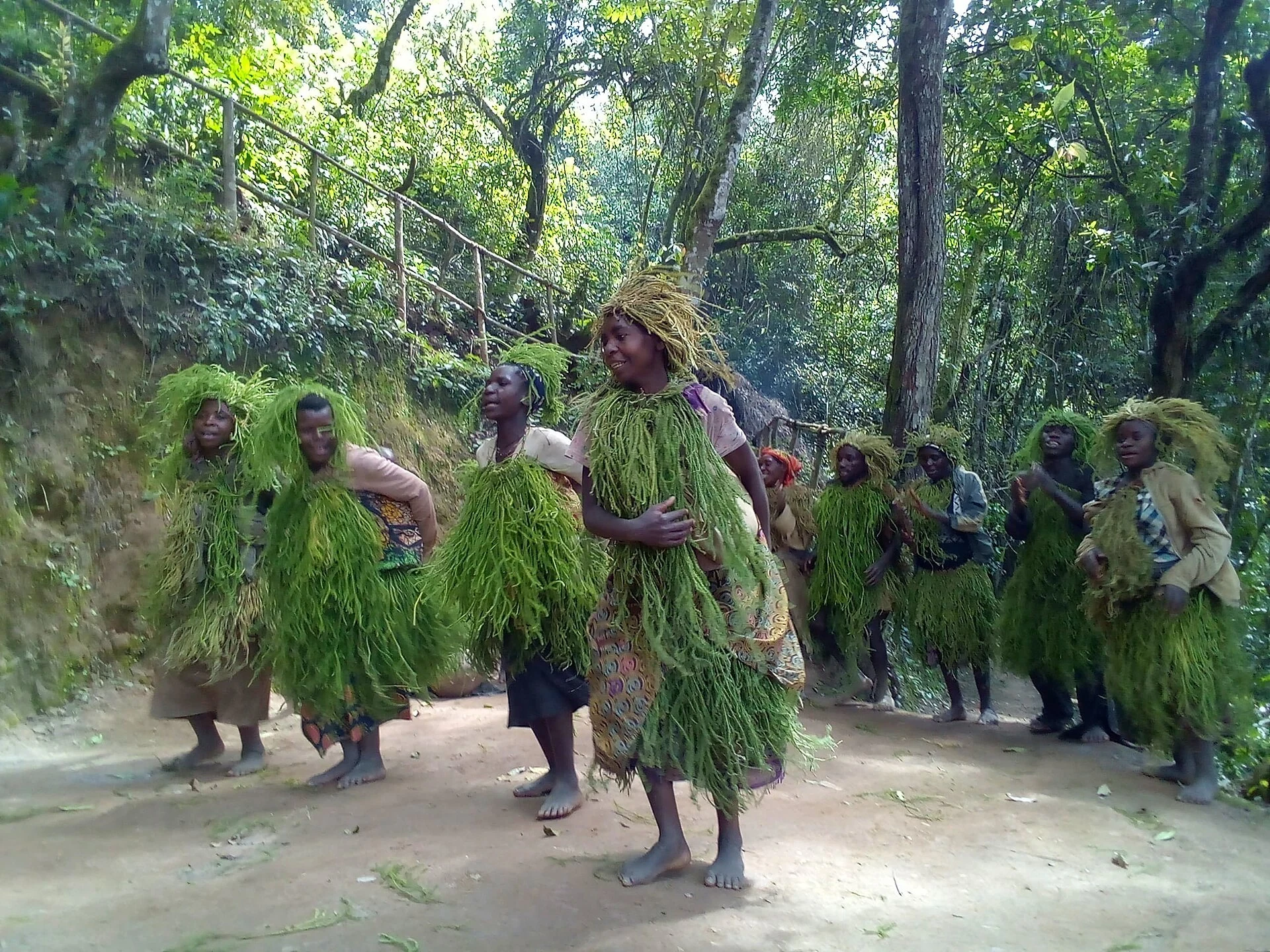 Batwa performers in grass costumes dancing in a forest clearing