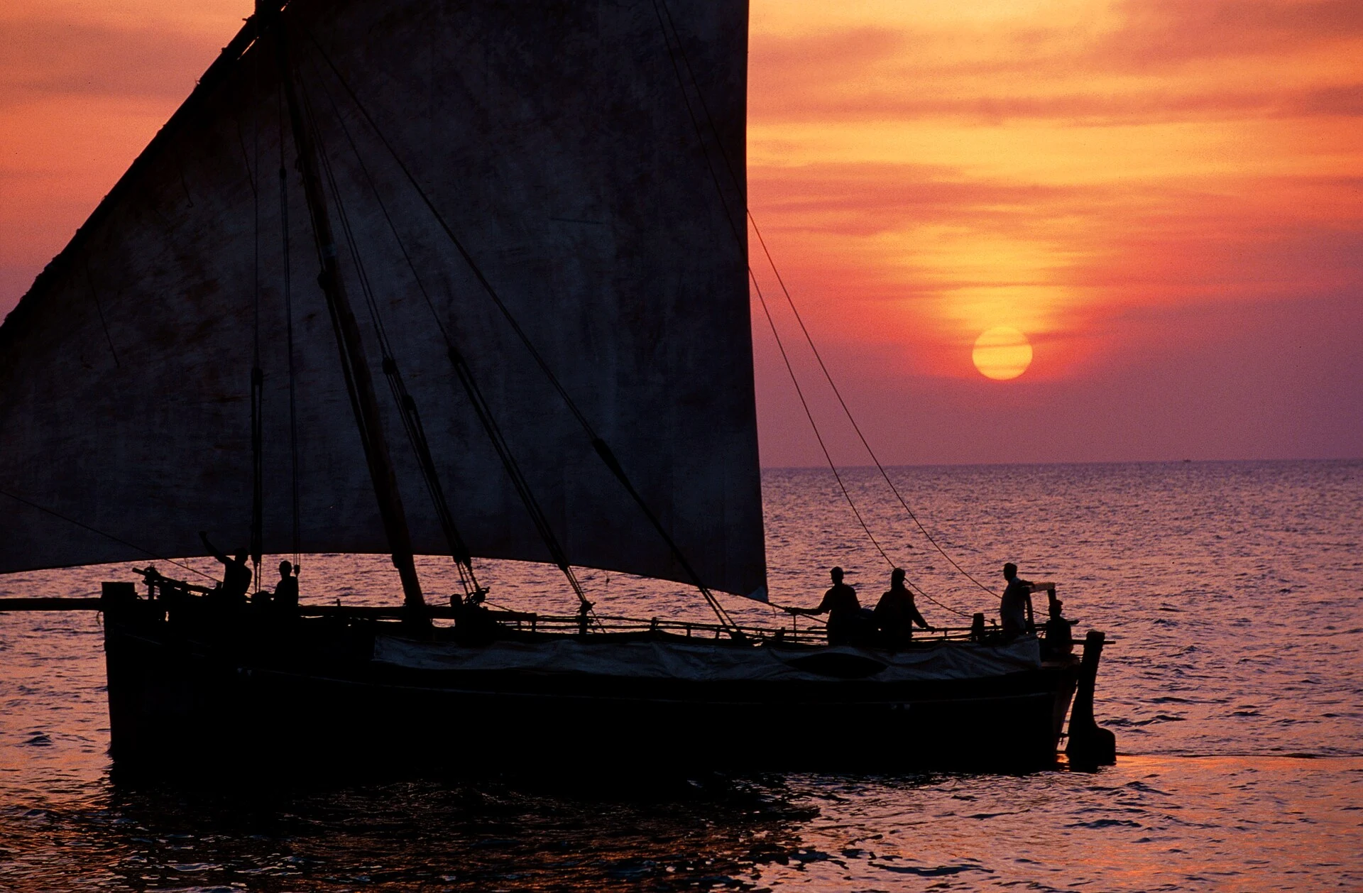 A dhow with passengers silhouetted against the sunset off Stone Town