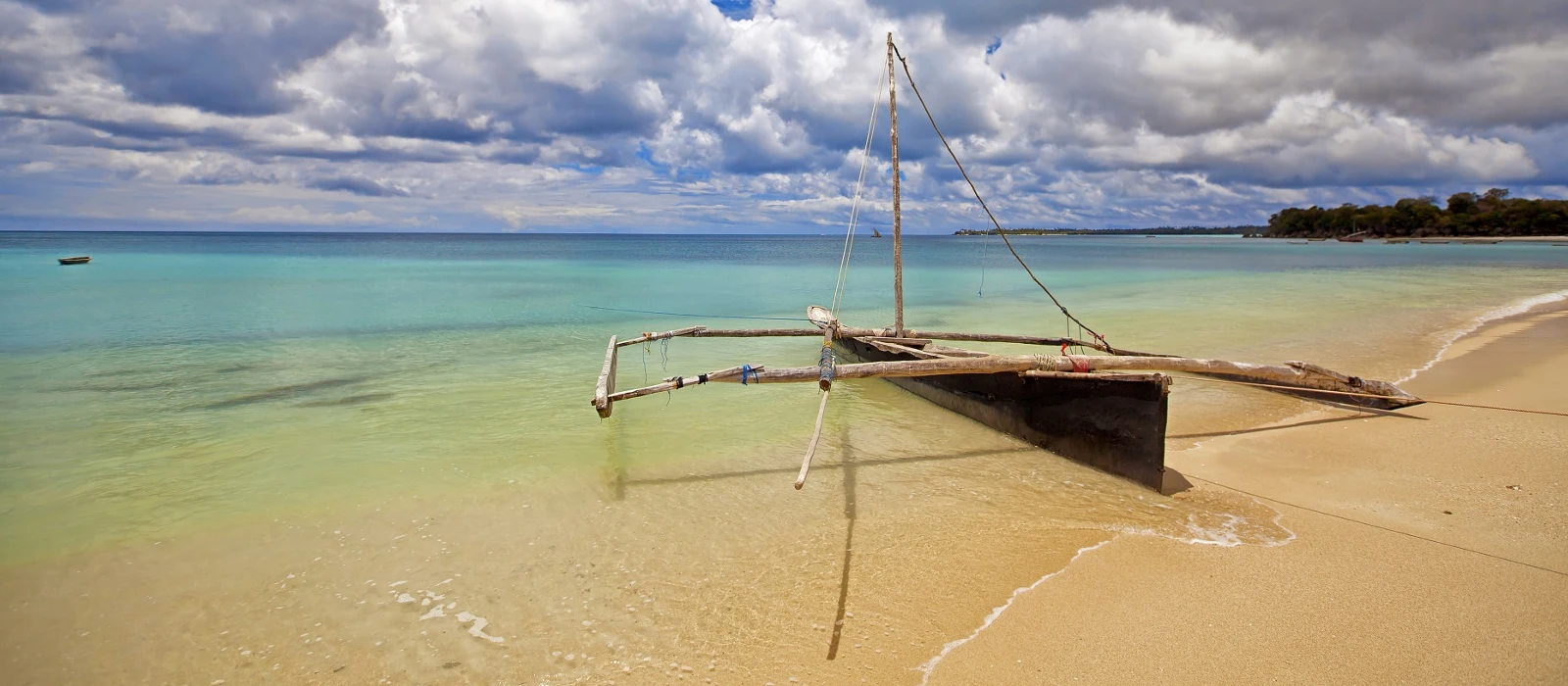 An outrigger boat resting in clear shallow water off a sandy beach