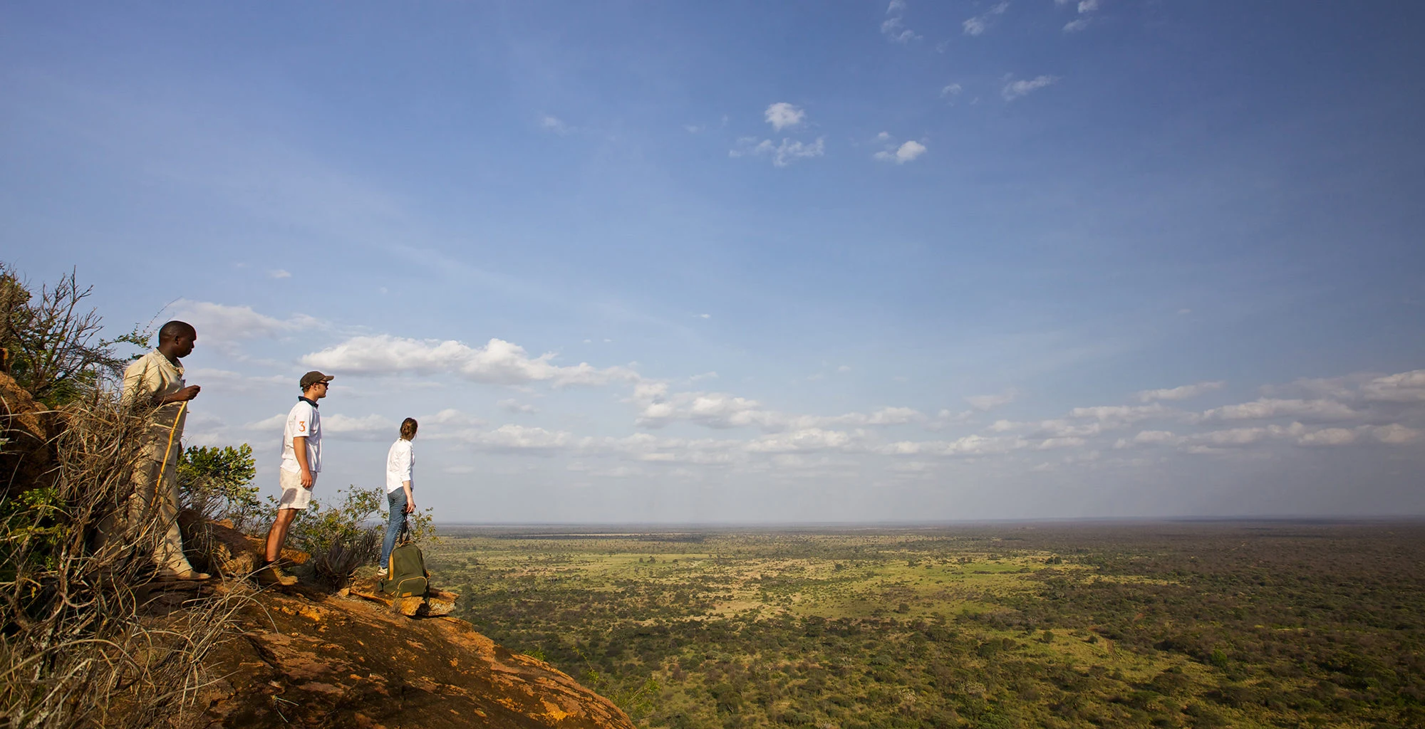 Guests on a rocky outcrop looking over the bush at sundowner time in Meru