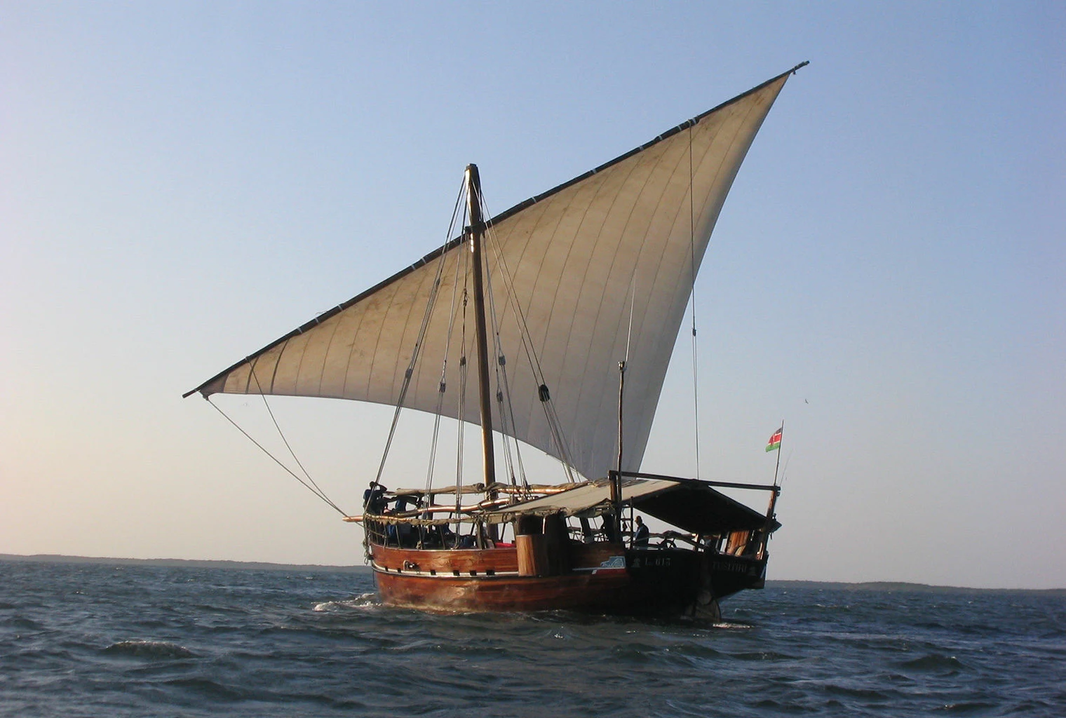 A traditional dhow under full sail on calm water