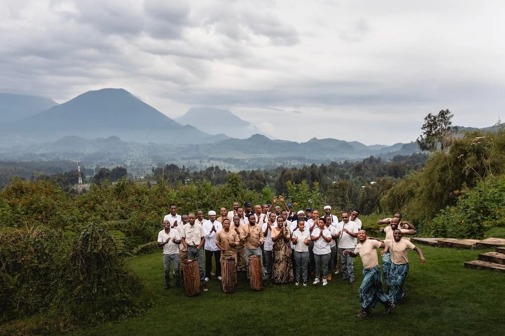A community choir performing on a lawn with the Virunga volcanoes behind