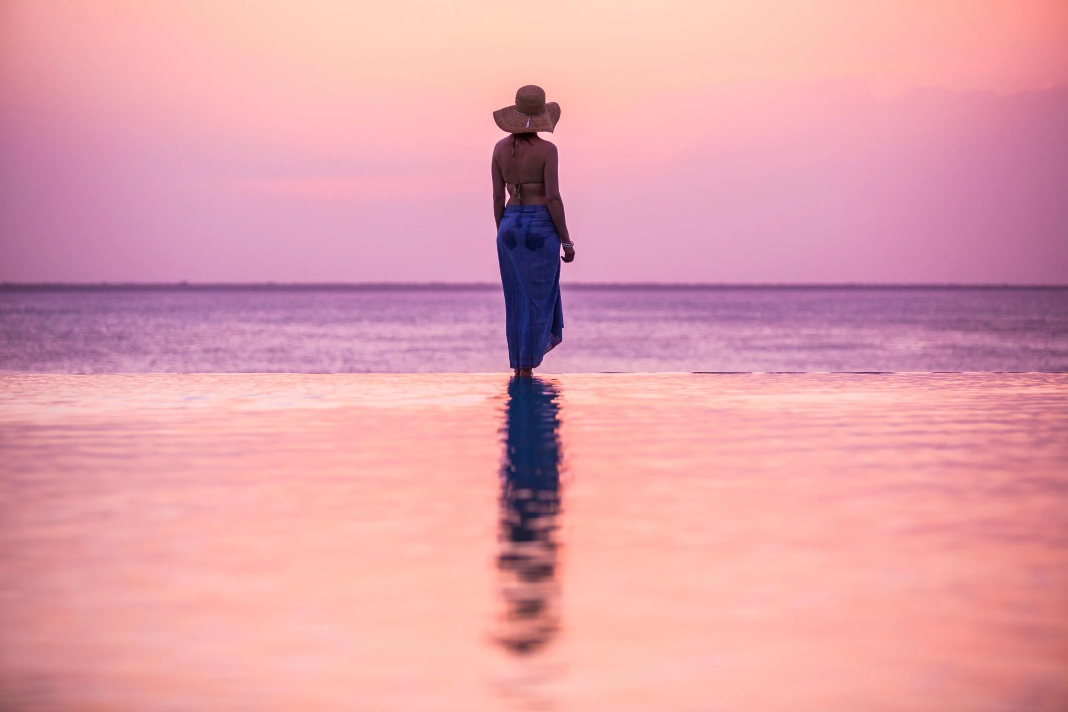 A distant figure standing on wet sand in pink evening light