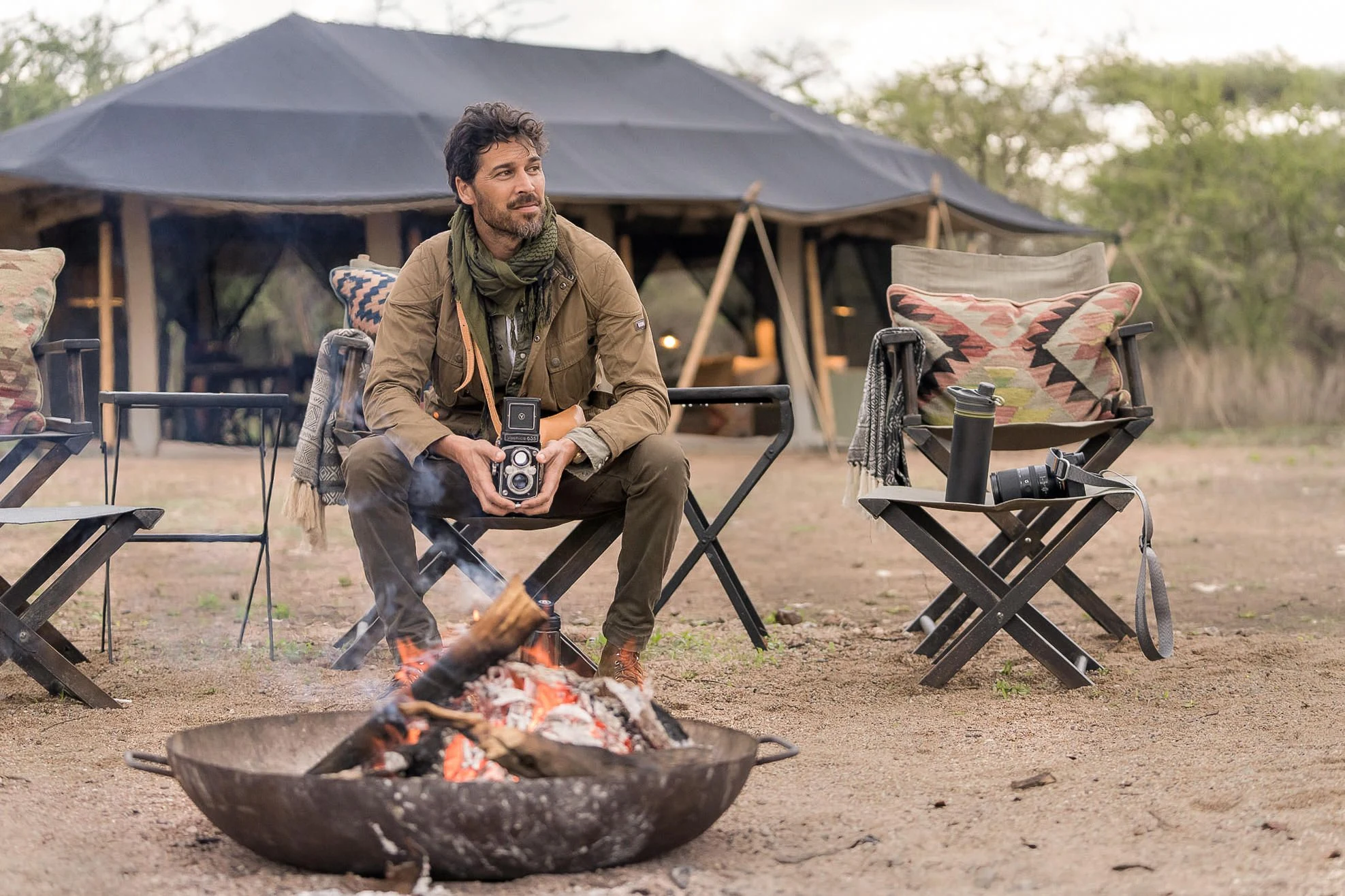 A guest with a camera by the campfire at Songa Migrational Camp, Kogatende