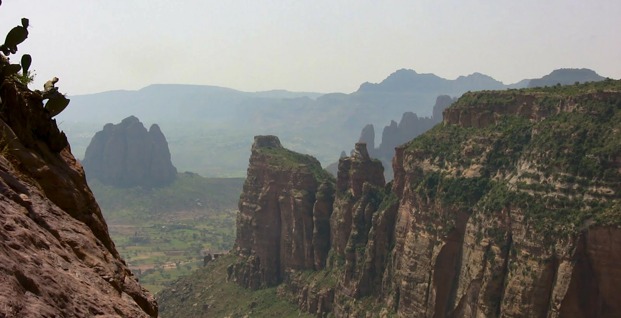Sandstone pinnacles and cliffs of the Gheralta massif above a green valley.