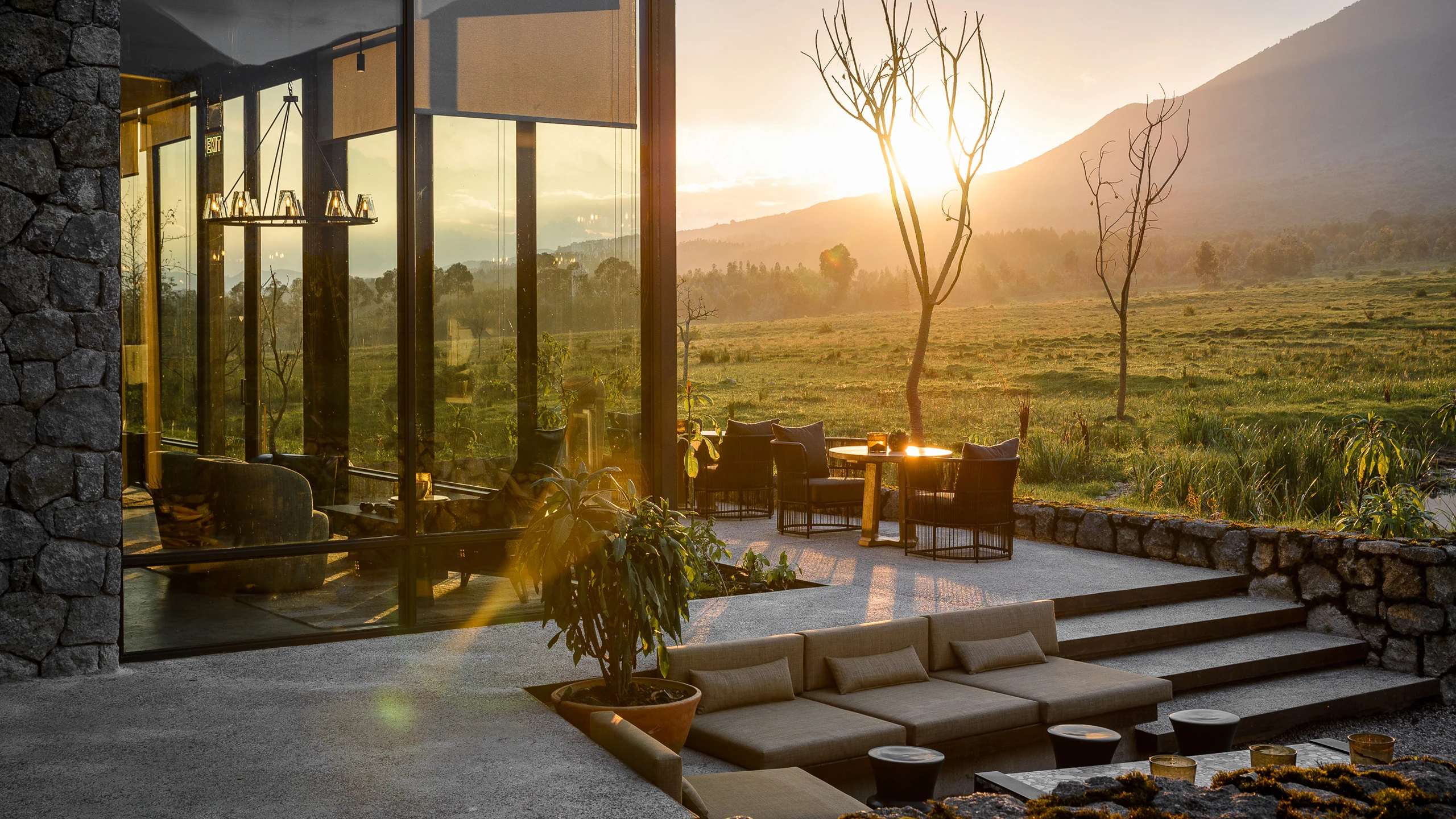 Lodge terrace with lounge seating, glass walls and volcano at sunset