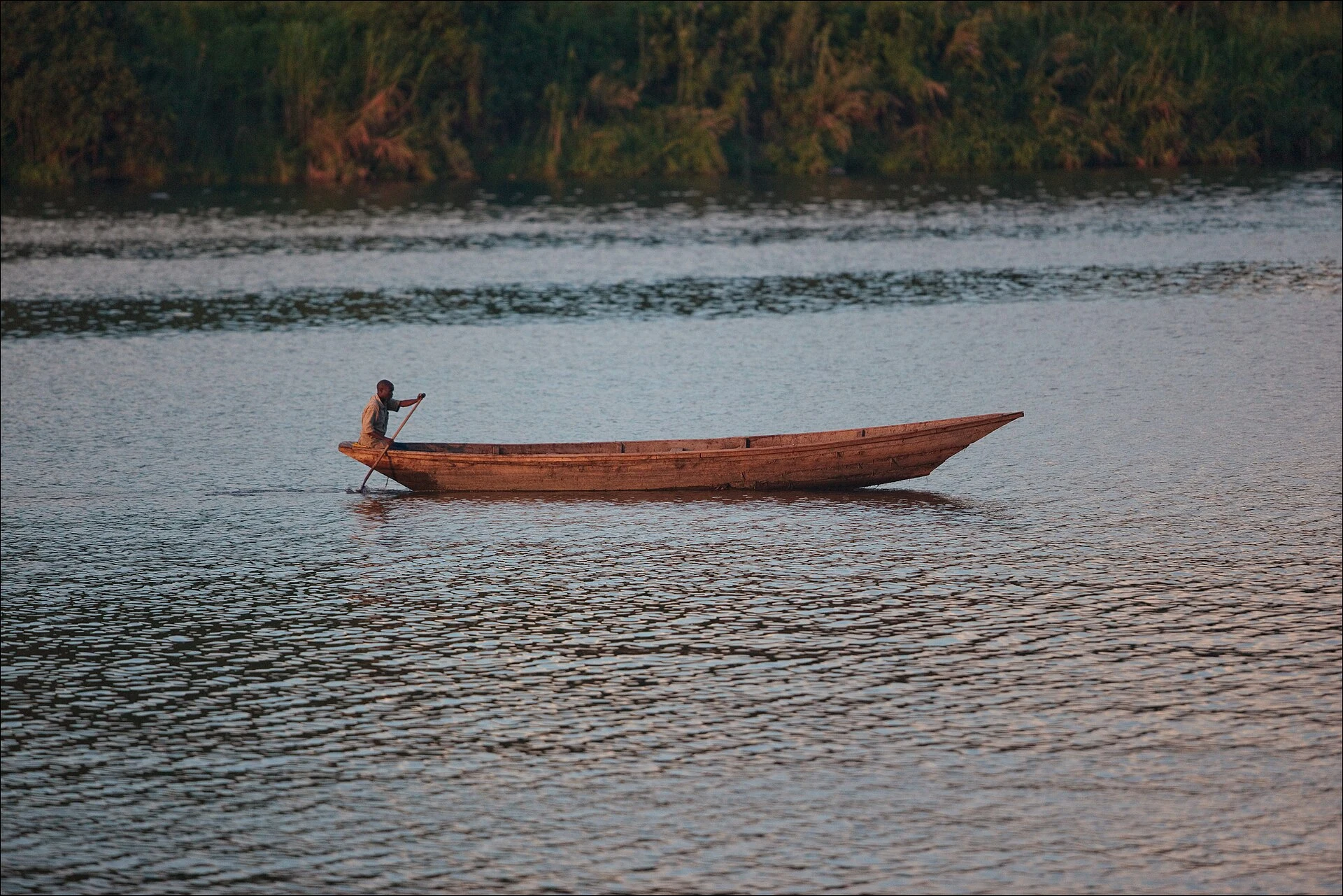 A man paddling a long wooden canoe on Lake Kivu in early morning light