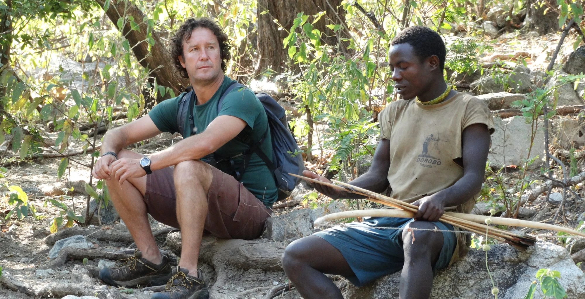 A visitor sitting and talking with a Hadza man on rocks