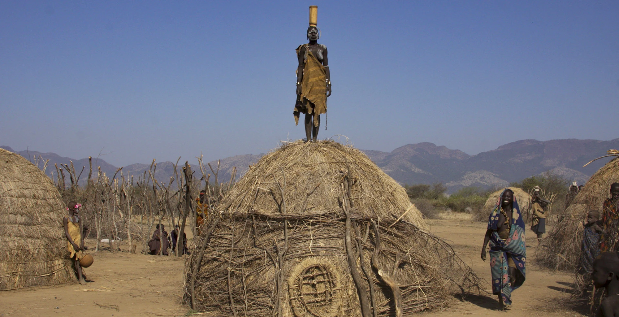 A man stands on top of a thatched hut in a dry Omo Valley village.