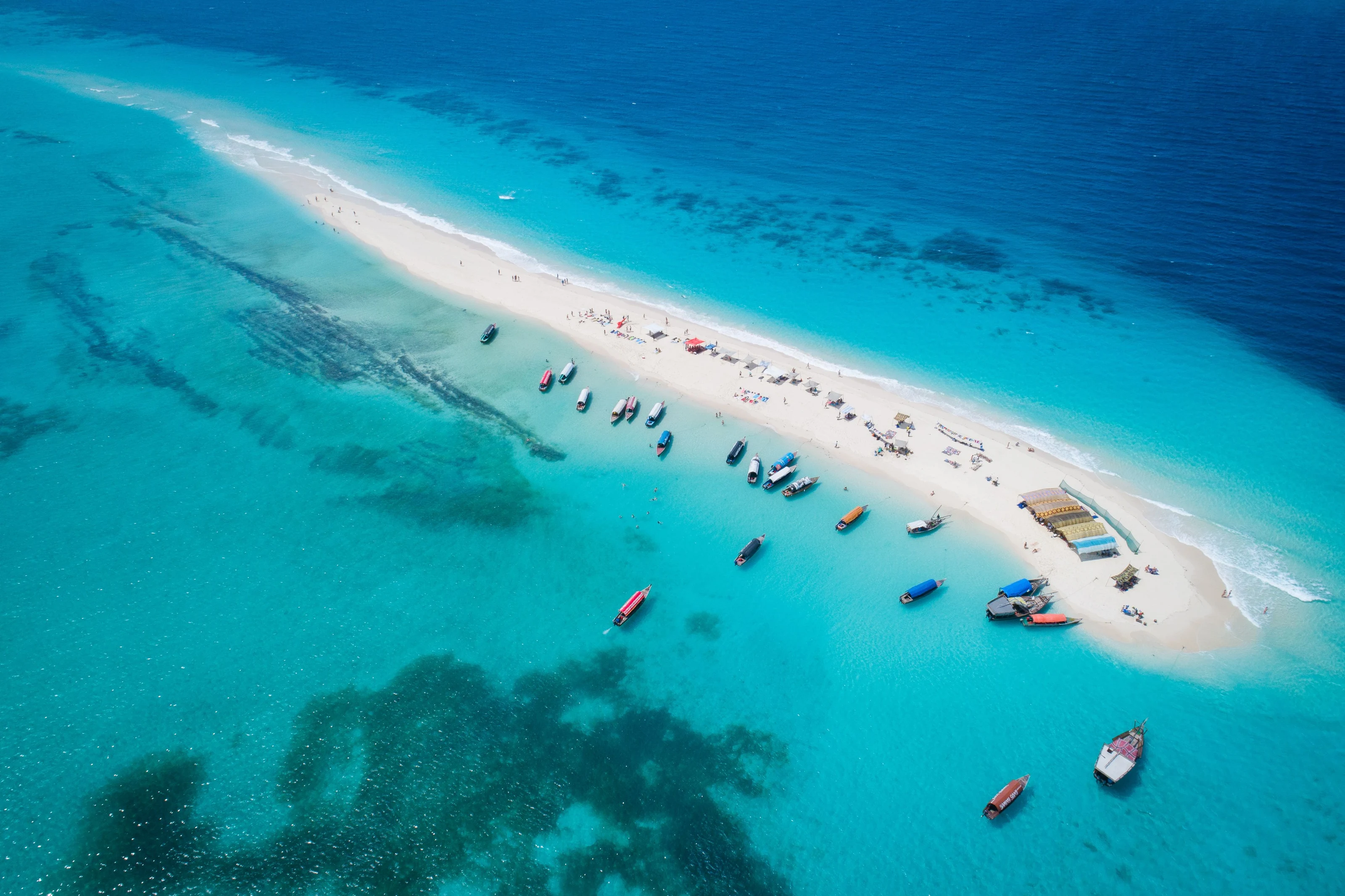 A white sandbank surrounded by turquoise water and boats