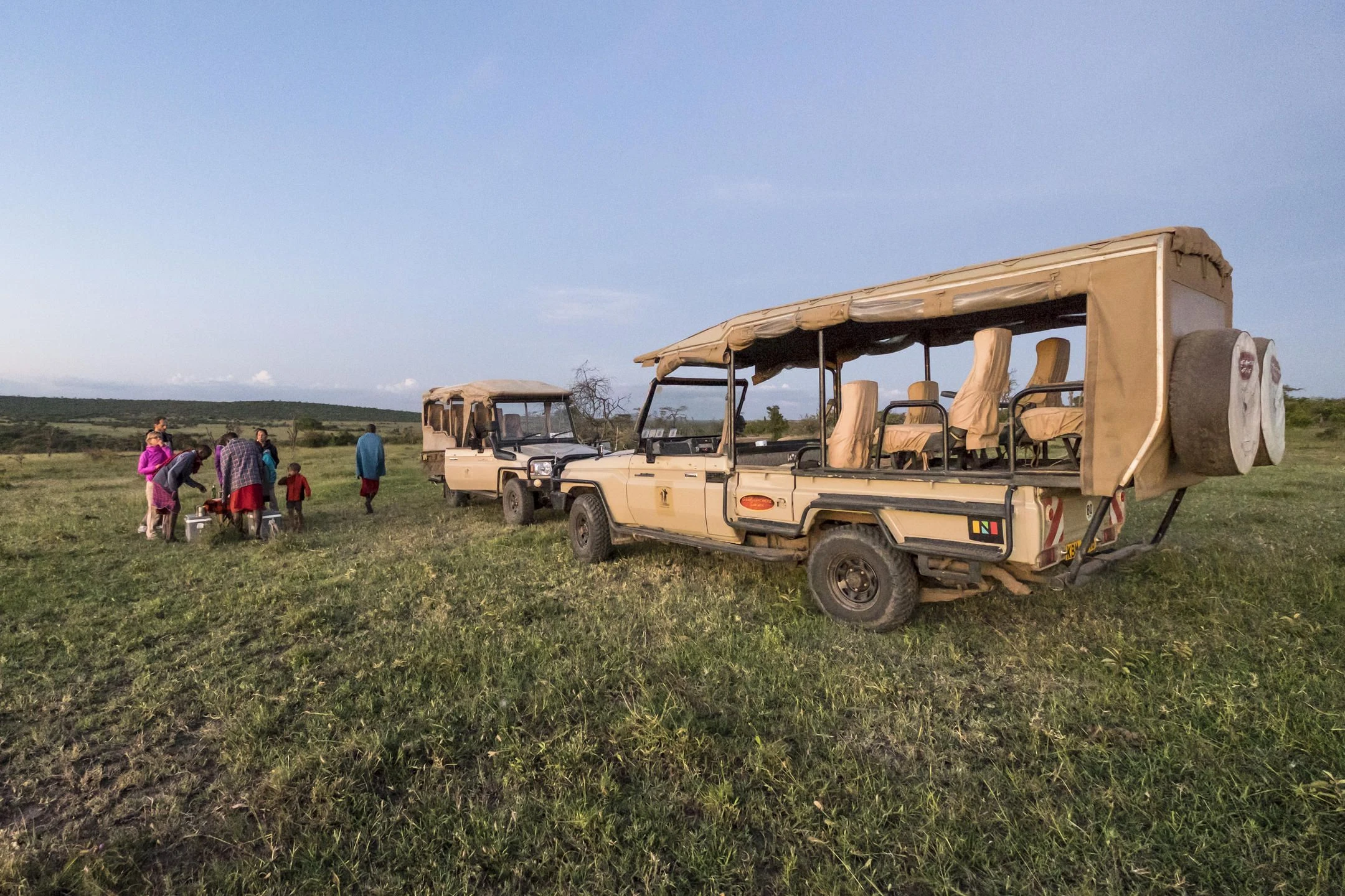Guests at a sundowner stop beside their safari vehicles in Ol Kinyei
