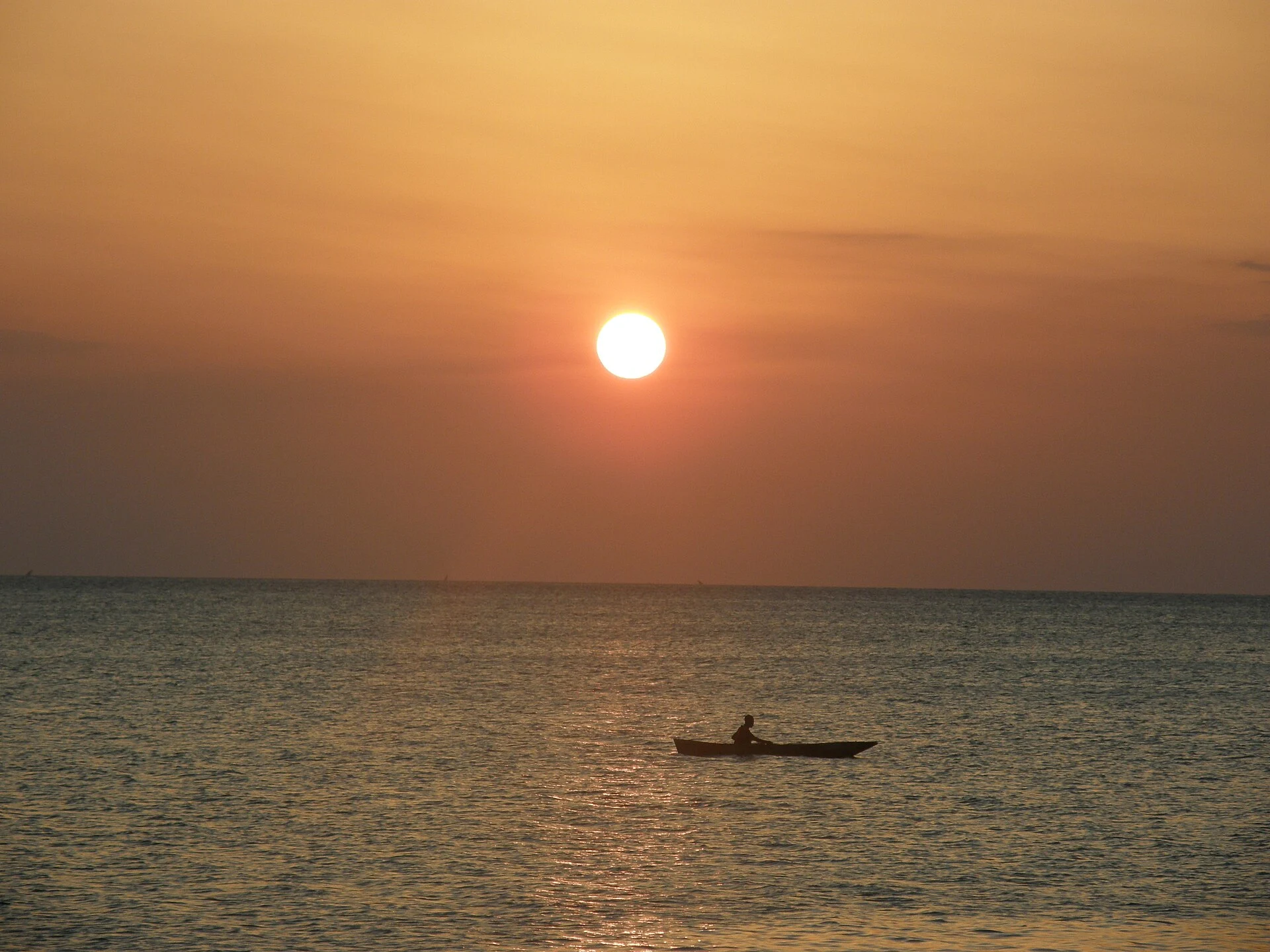 The sun setting over a calm sea off Zanzibar with a small boat