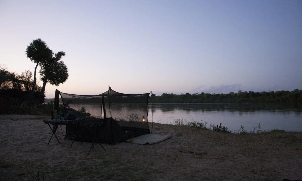 A netted fly camp bed on a riverbank at dusk in Selous