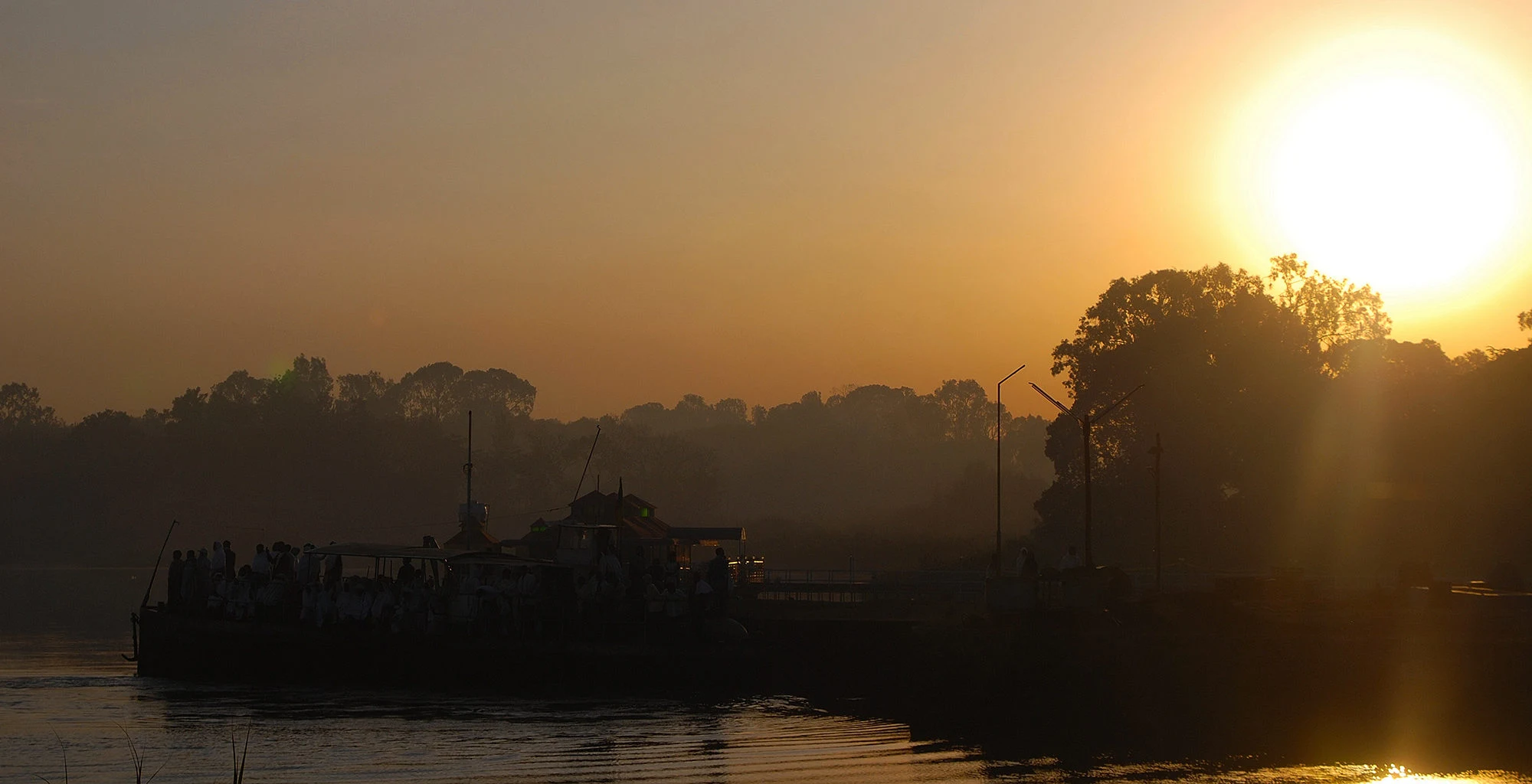 The sun sets behind trees and a jetty on the water at Bahir Dar.