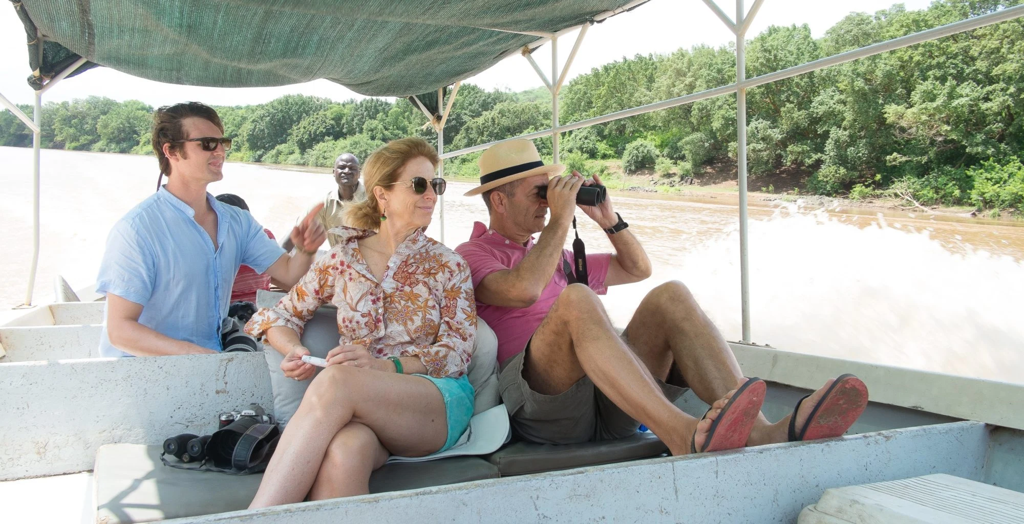 Visitors with a camera and binoculars ride a boat on the Omo River.