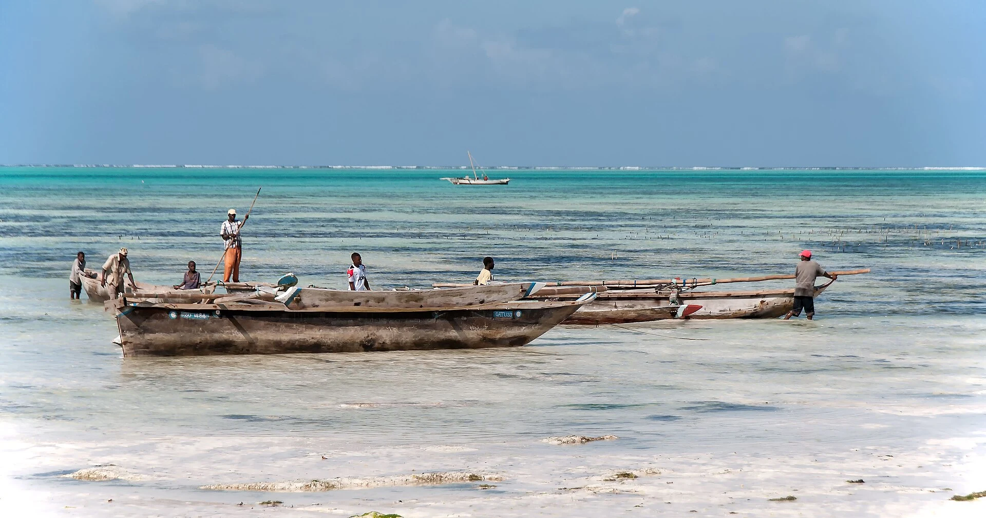 Fishermen with a wooden boat in shallow turquoise water off Zanzibar