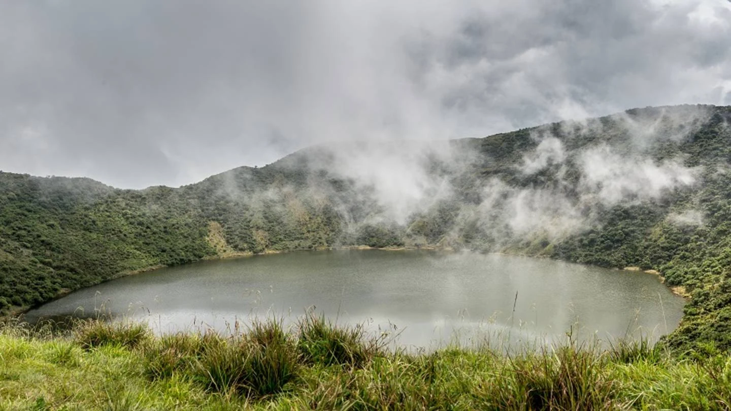 The crater lake inside Bisoke volcano, ringed by green slopes and cloud