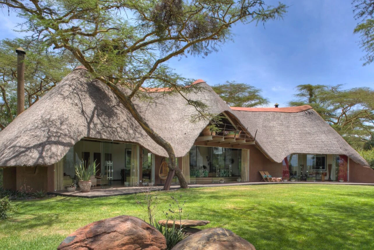 Thatched lodge beside a green lawn at Solio Lodge