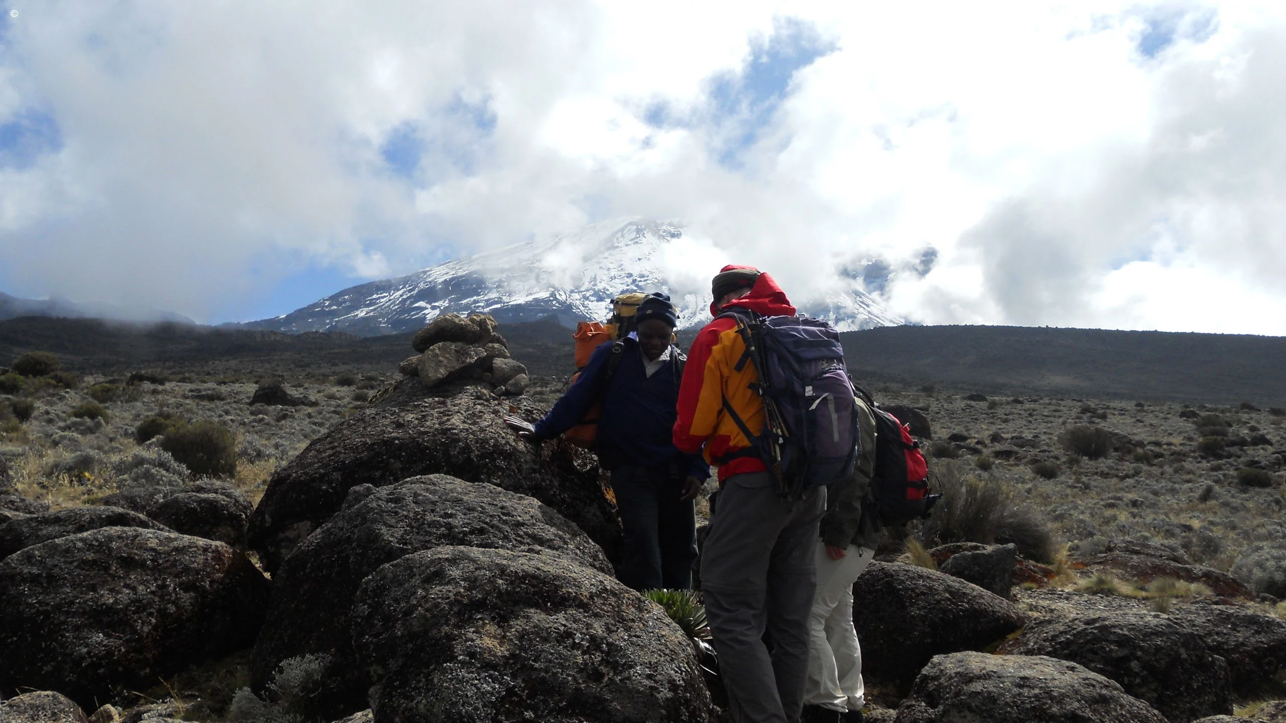 Trekkers with backpacks crossing rocky ground on Kilimanjaro