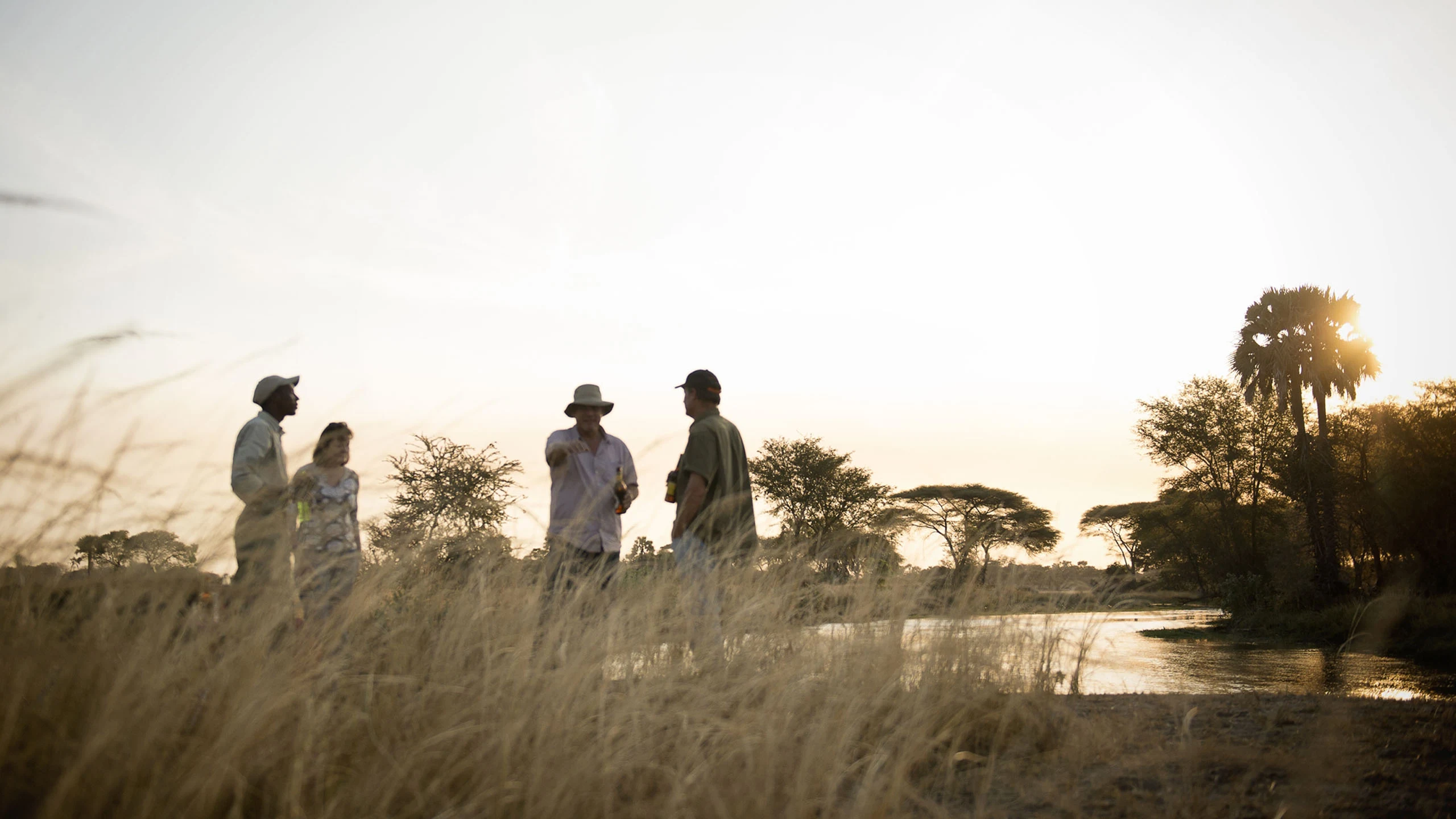 Walking safari group silhouetted beside a river at golden hour in Katavi