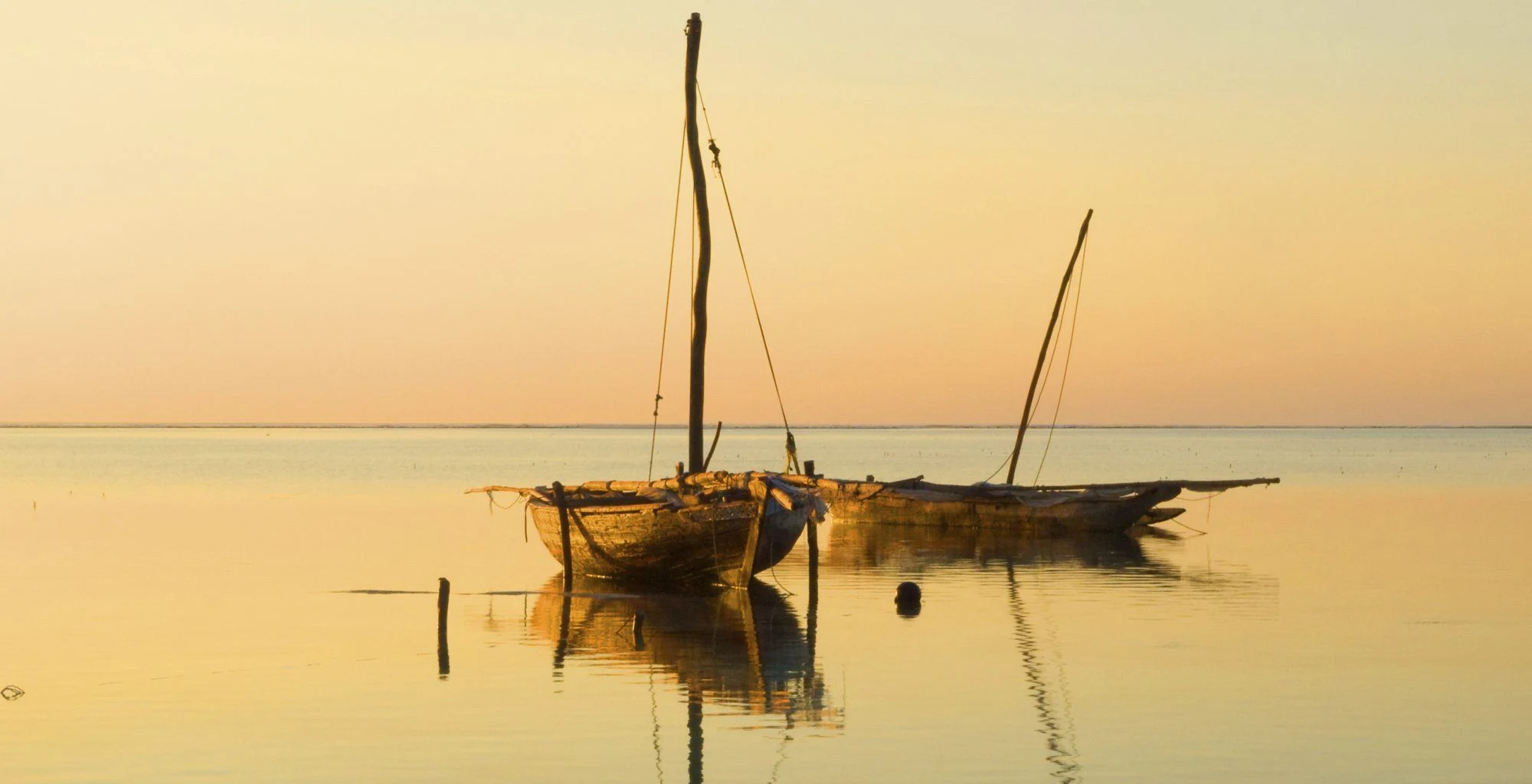 A dhow at anchor on glassy water under a soft golden sky