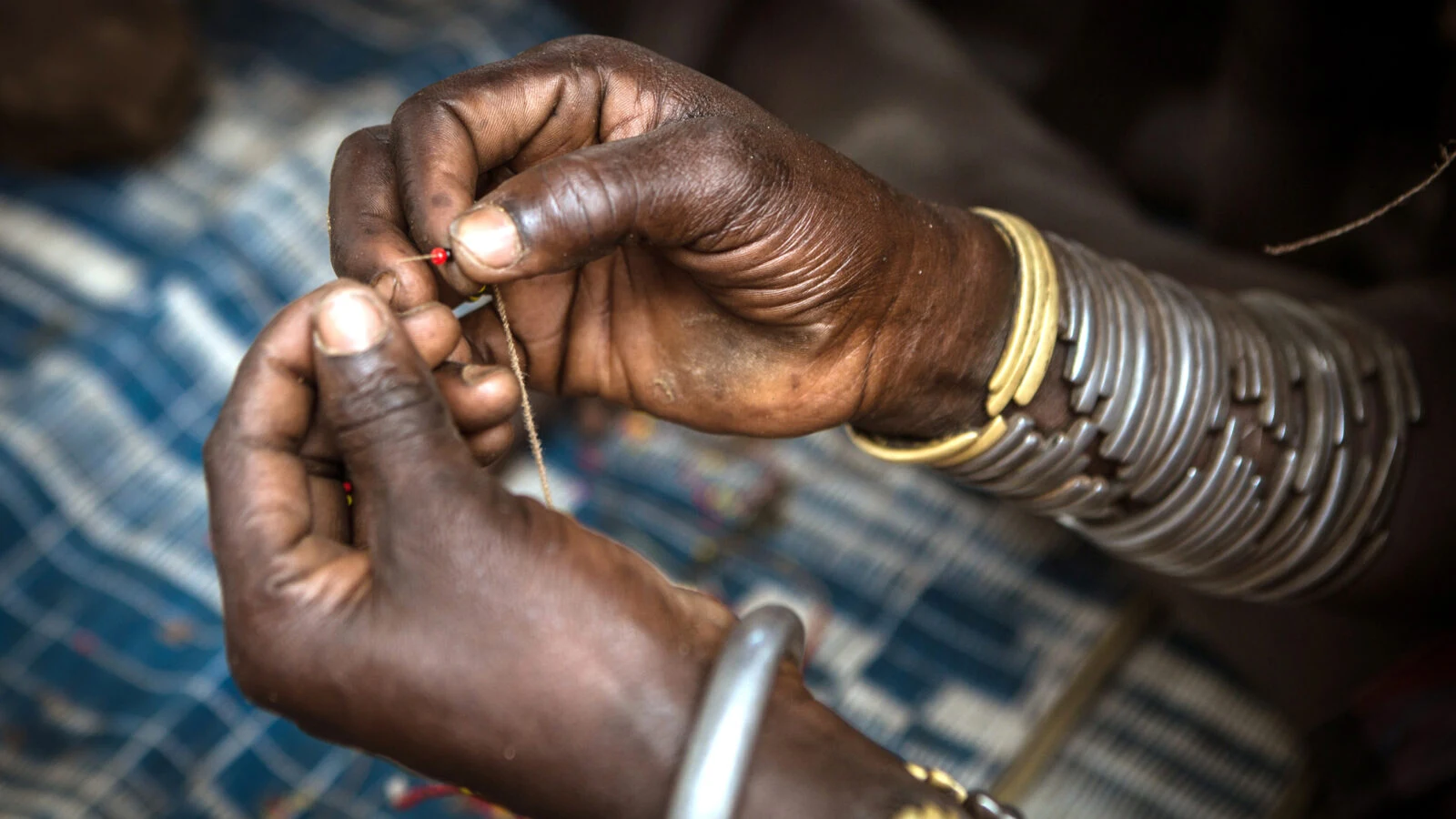 Hands threading small beads with metal bracelets on the wrist