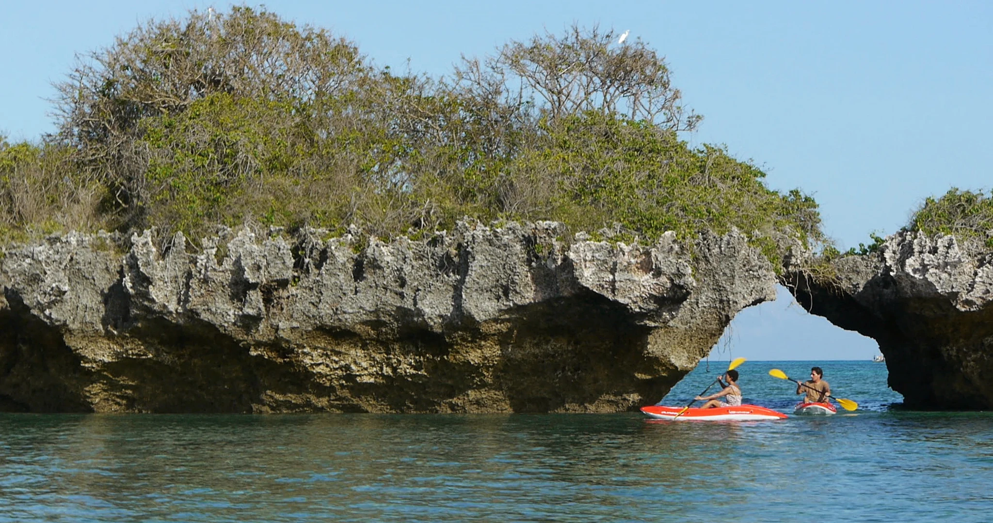 Kayakers paddling beneath a rocky islet