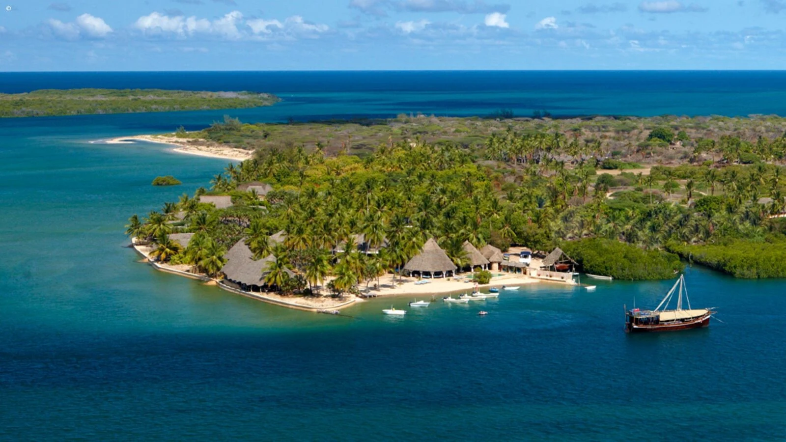 Palm-covered island with thatched buildings and a dhow moored off the Kenyan coast