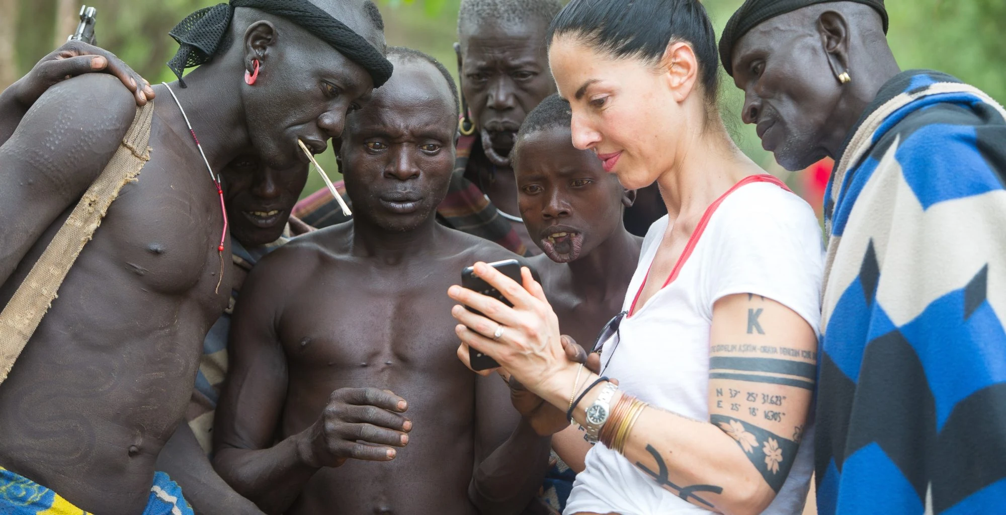 A visitor shows photos on her phone to a group of Mursi men.