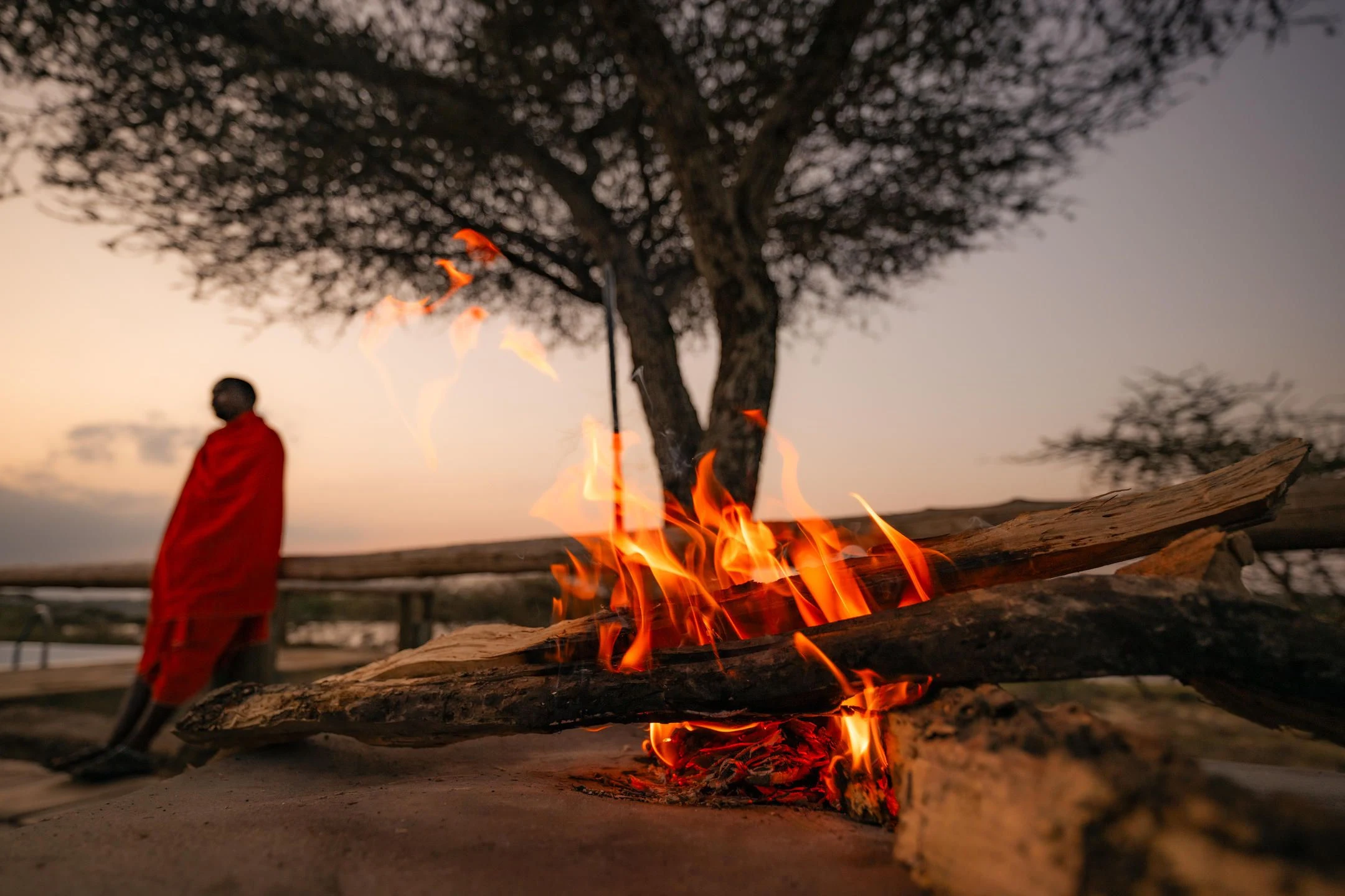A Maasai man standing beside a campfire at dusk