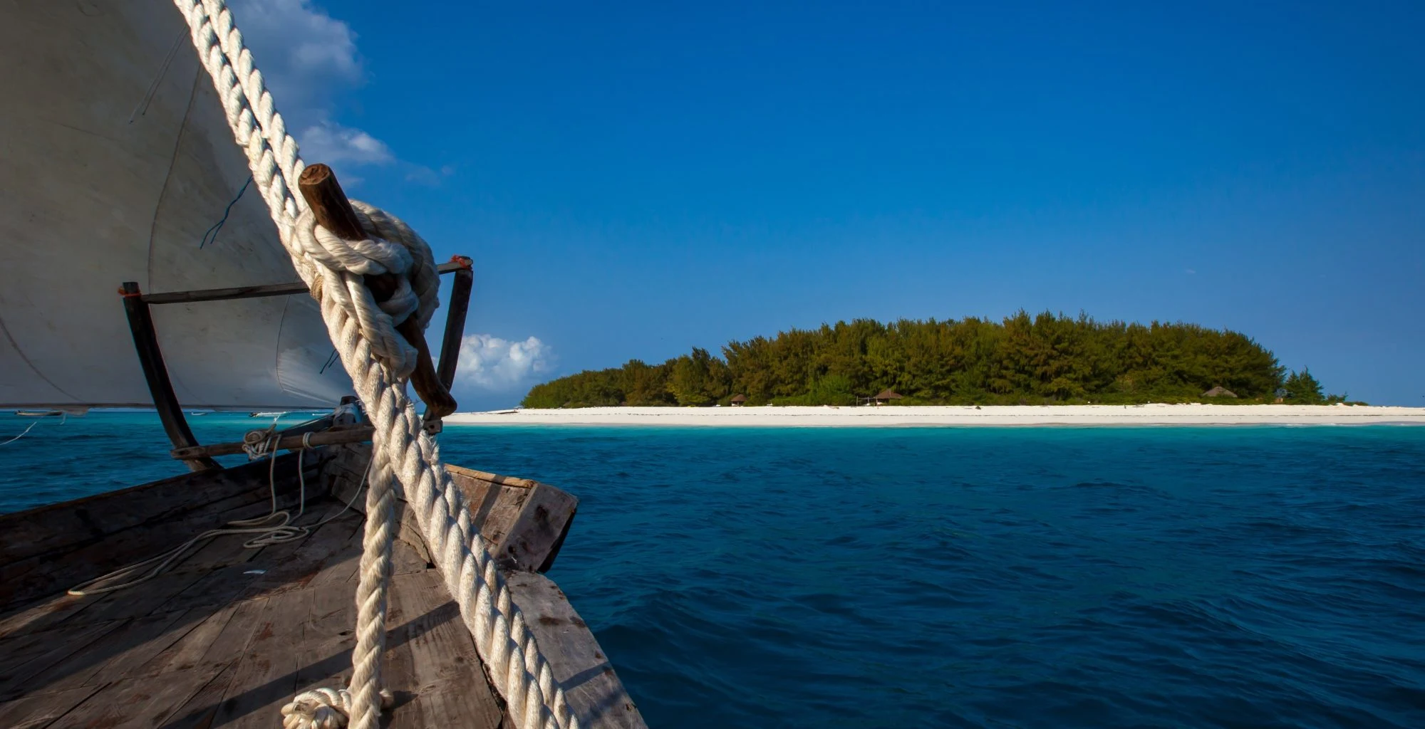 The bow of a dhow sailing toward a small, low island fringed with sand