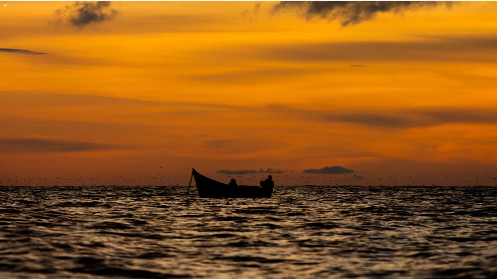 Fishing canoe silhouetted on a lake under an orange sunset