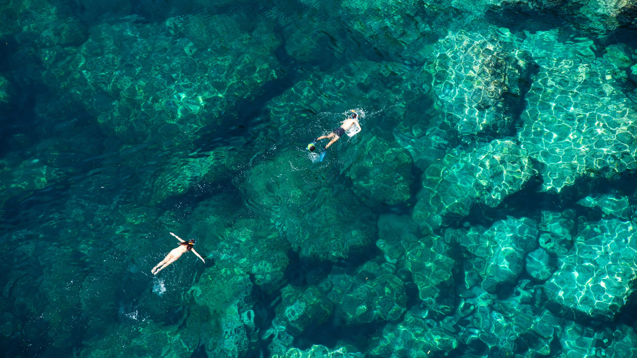 Two snorkellers floating above a shallow coral reef, seen from above