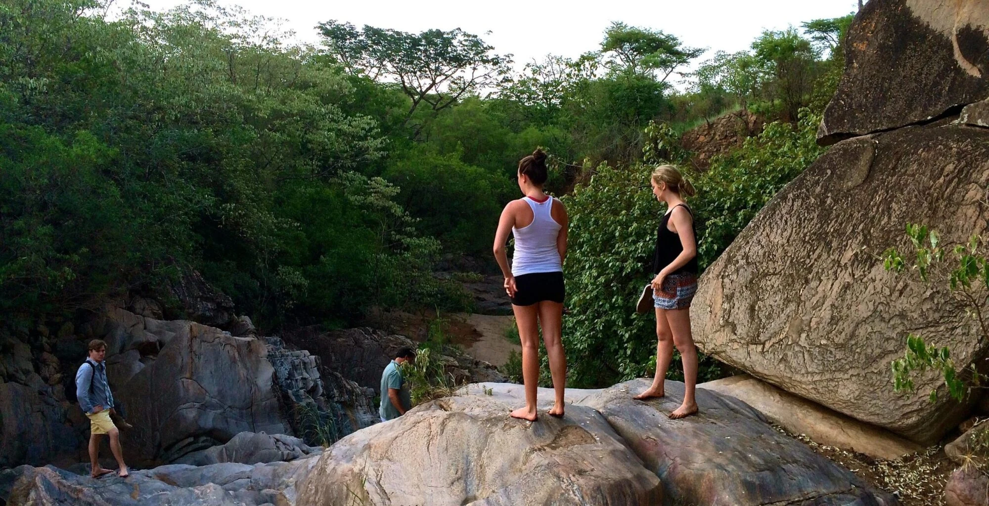 Walkers standing on boulders above a rocky stream bed in Kidepo Valley