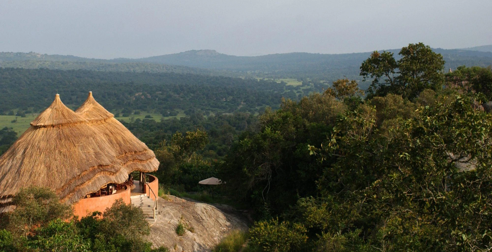 Thatched lodge on a rocky outcrop above wooded hills at Mihingo Lodge