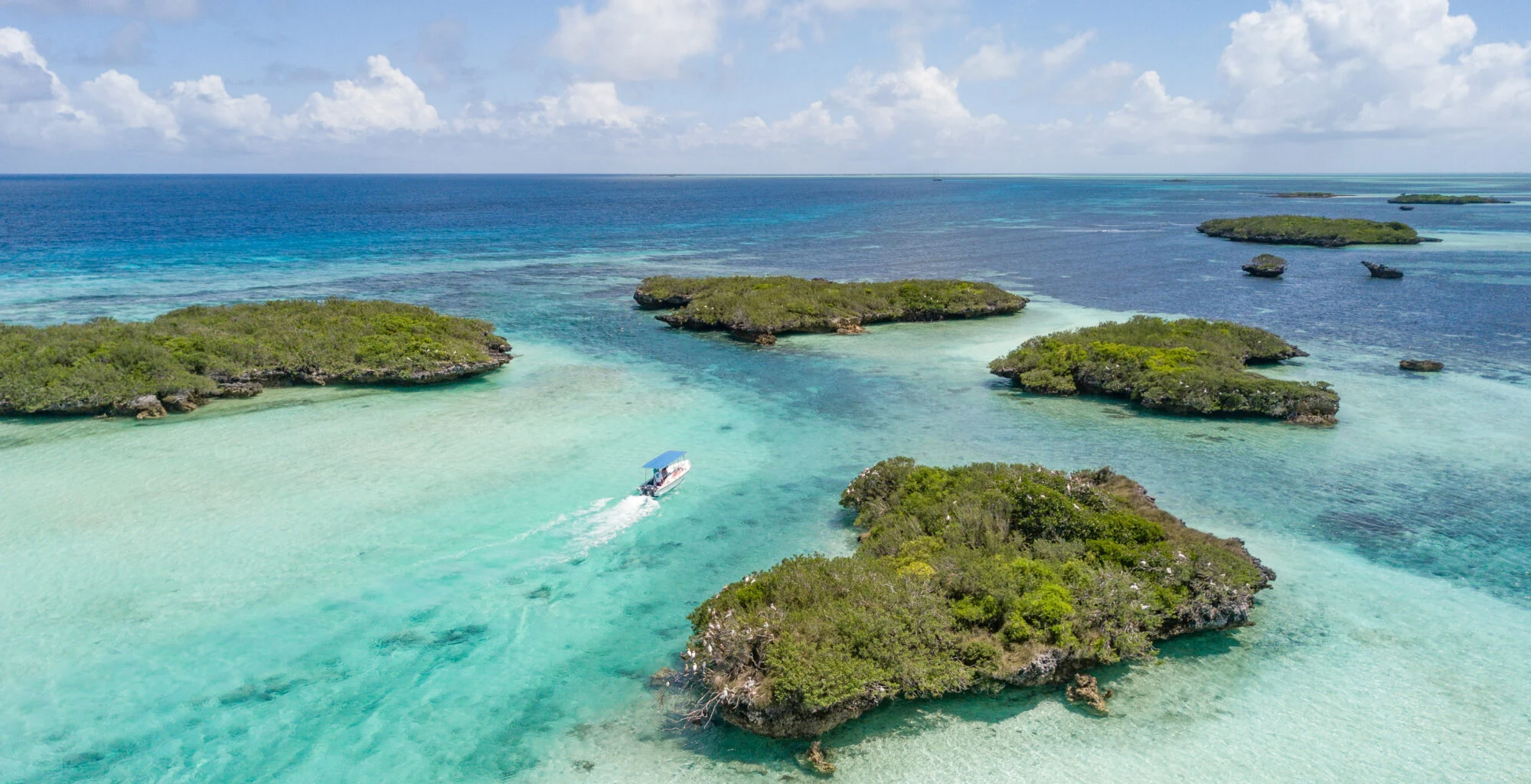 A small fishing boat speeding across shallow water between low green islands