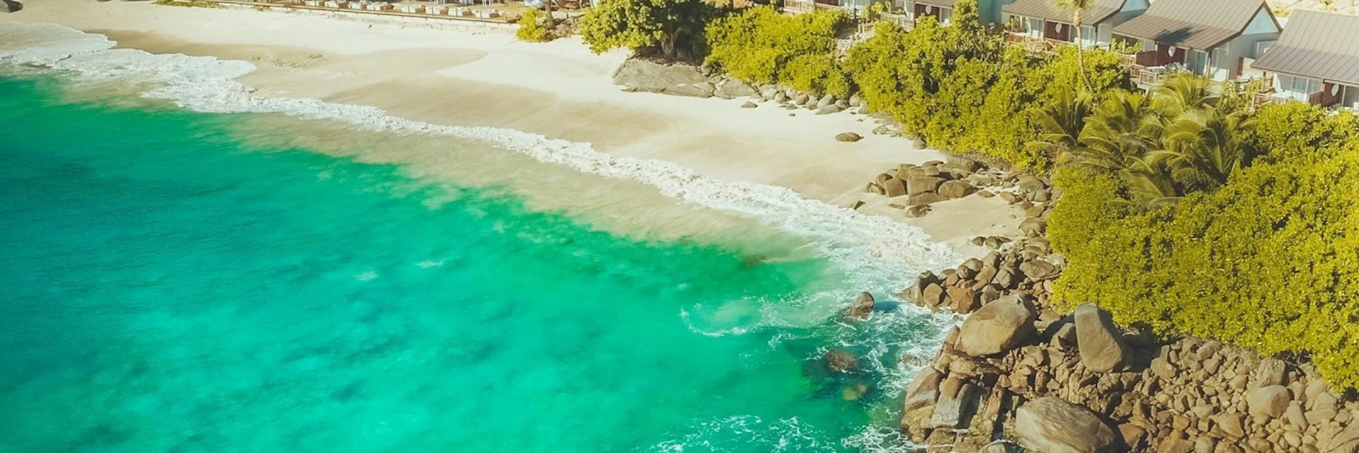 A small cove of white sand and turquoise water below green hills