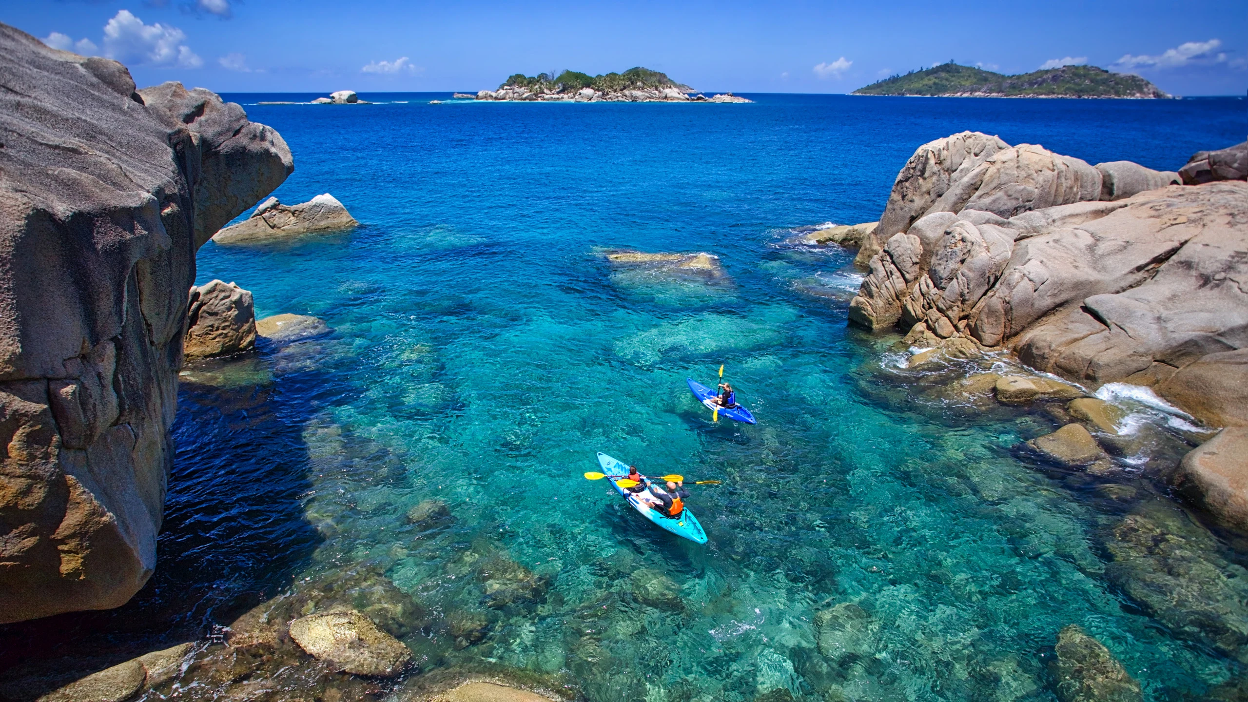 Two kayakers paddling through clear water between granite boulders