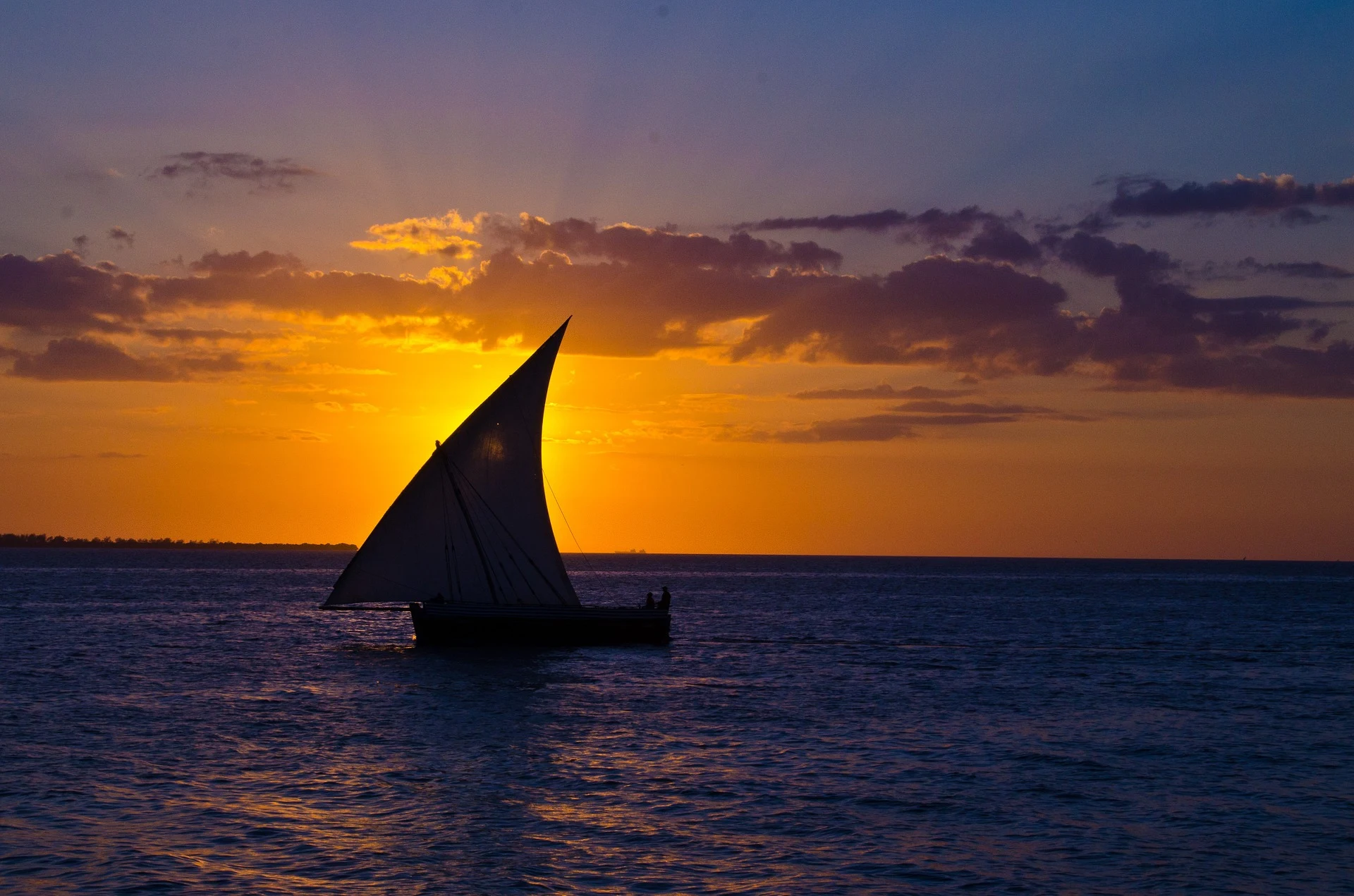 A dhow silhouetted against an orange sunset over the sea in Zanzibar