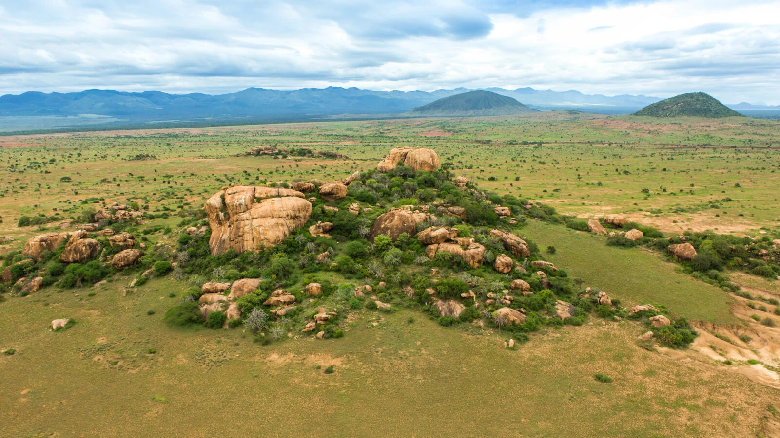 Aerial of rocky outcrops on green hillock in open plain, distant hills