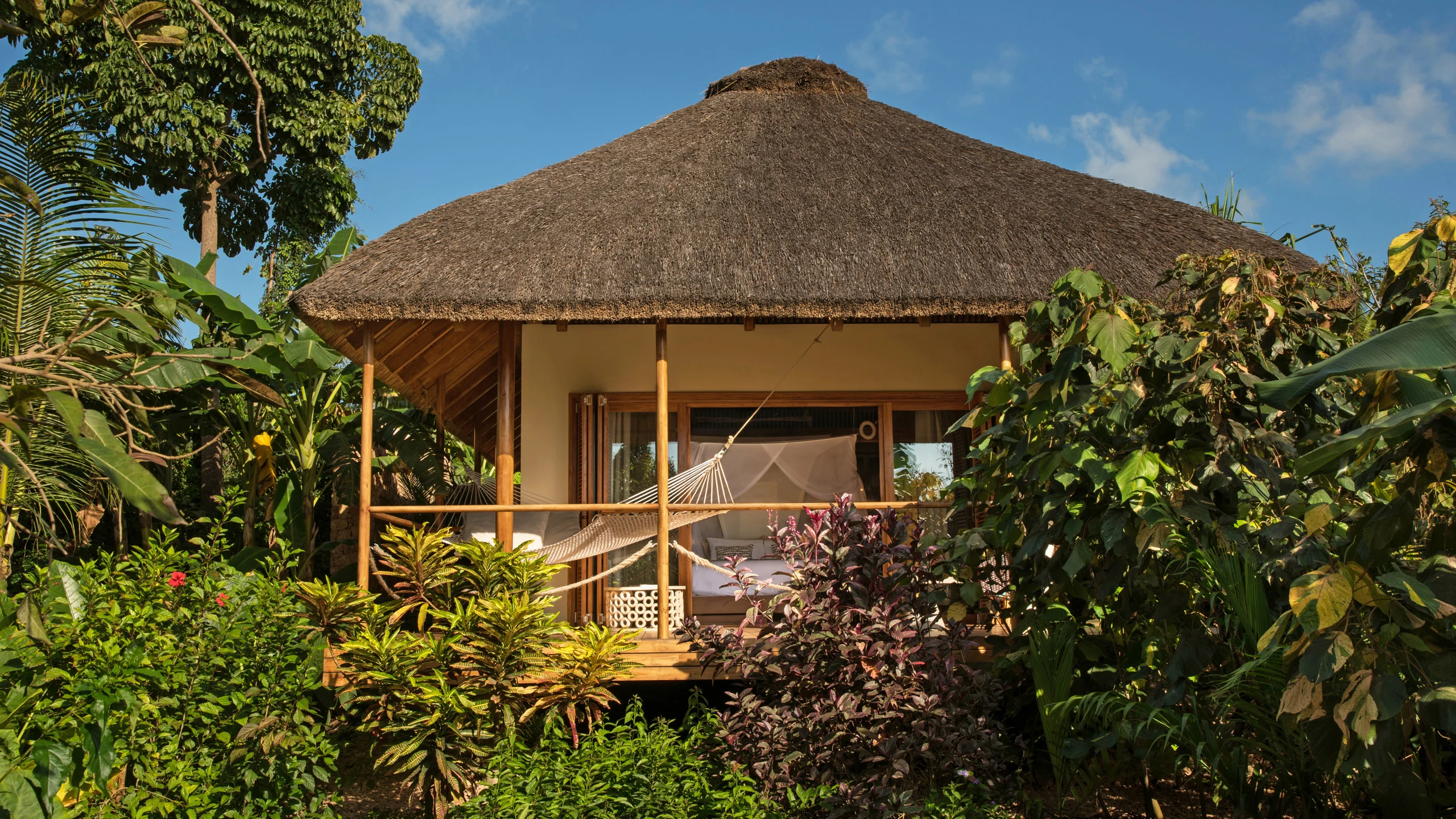 Thatched bungalow with deck among green and purple foliage at Zuri Zanzibar