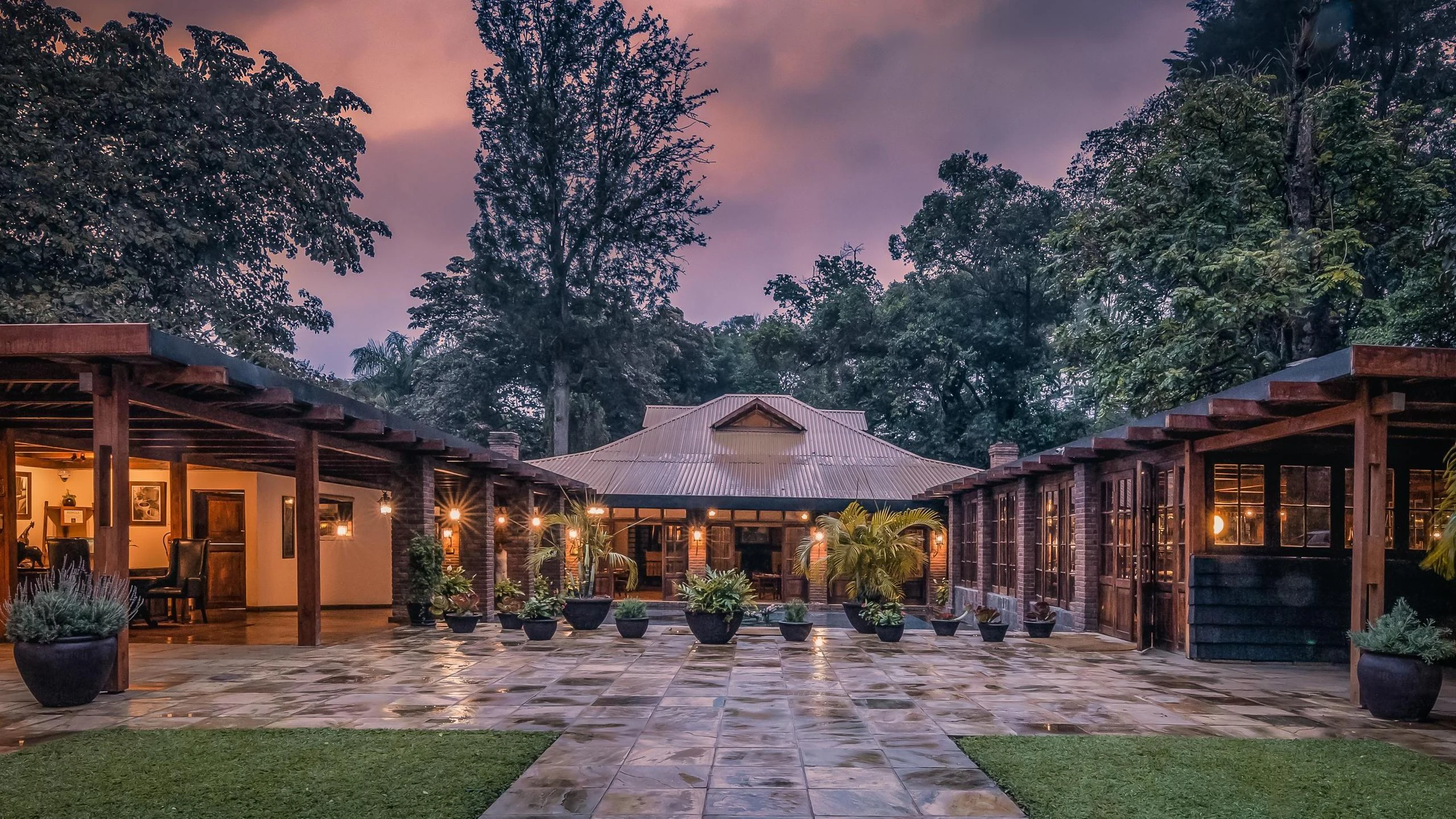 Lit stone courtyard of a lodge reception under a purple sunset at Arusha Coffee Lodge