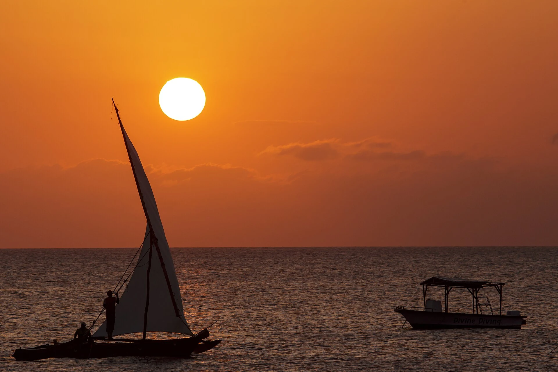 A dhow and a small motorboat silhouetted against a Zanzibar sunset