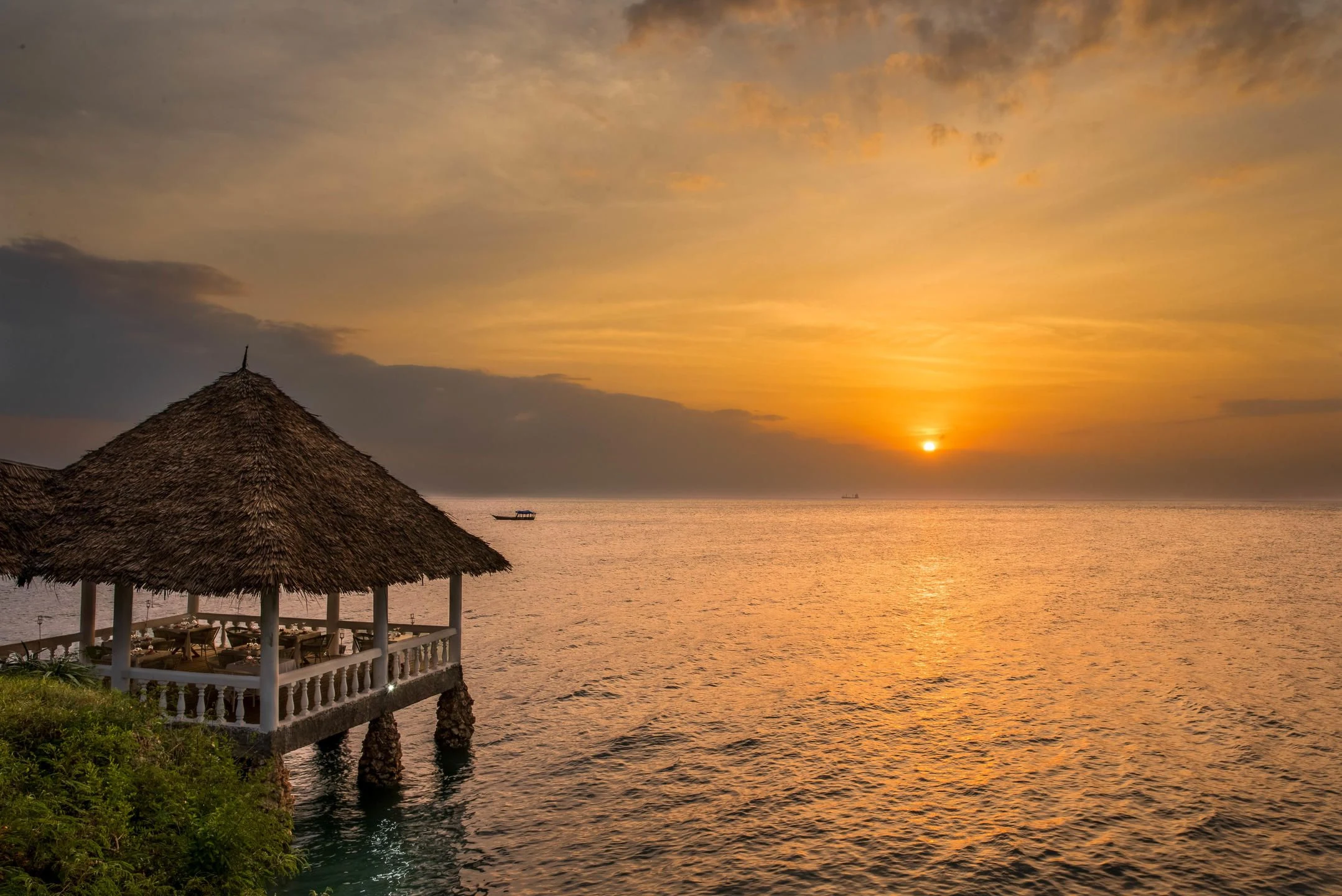 The sun setting over the sea beside a thatched pavilion on stilts