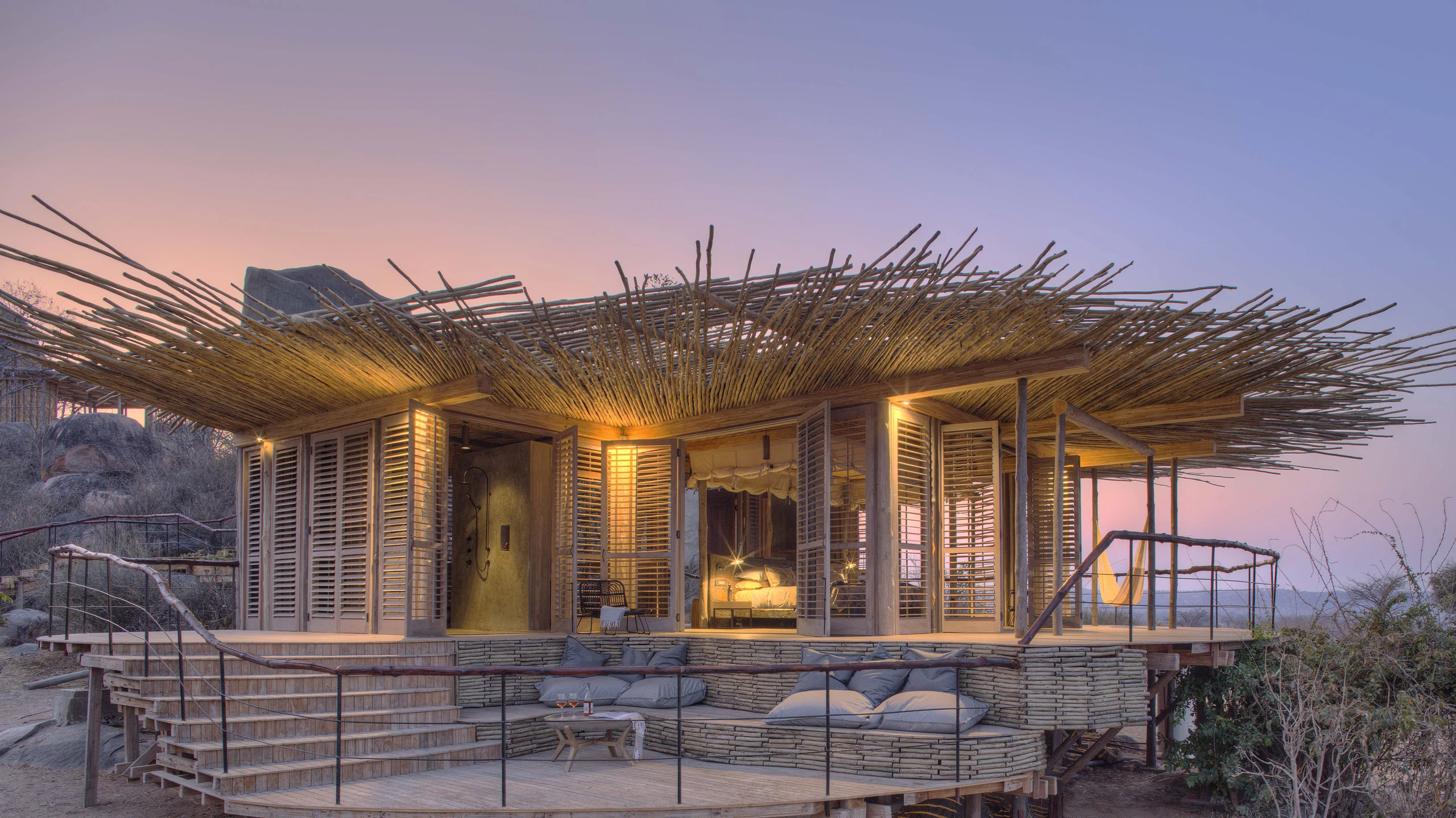 Lodge with a woven projecting roof among granite boulders at dusk, Jabali Ridge