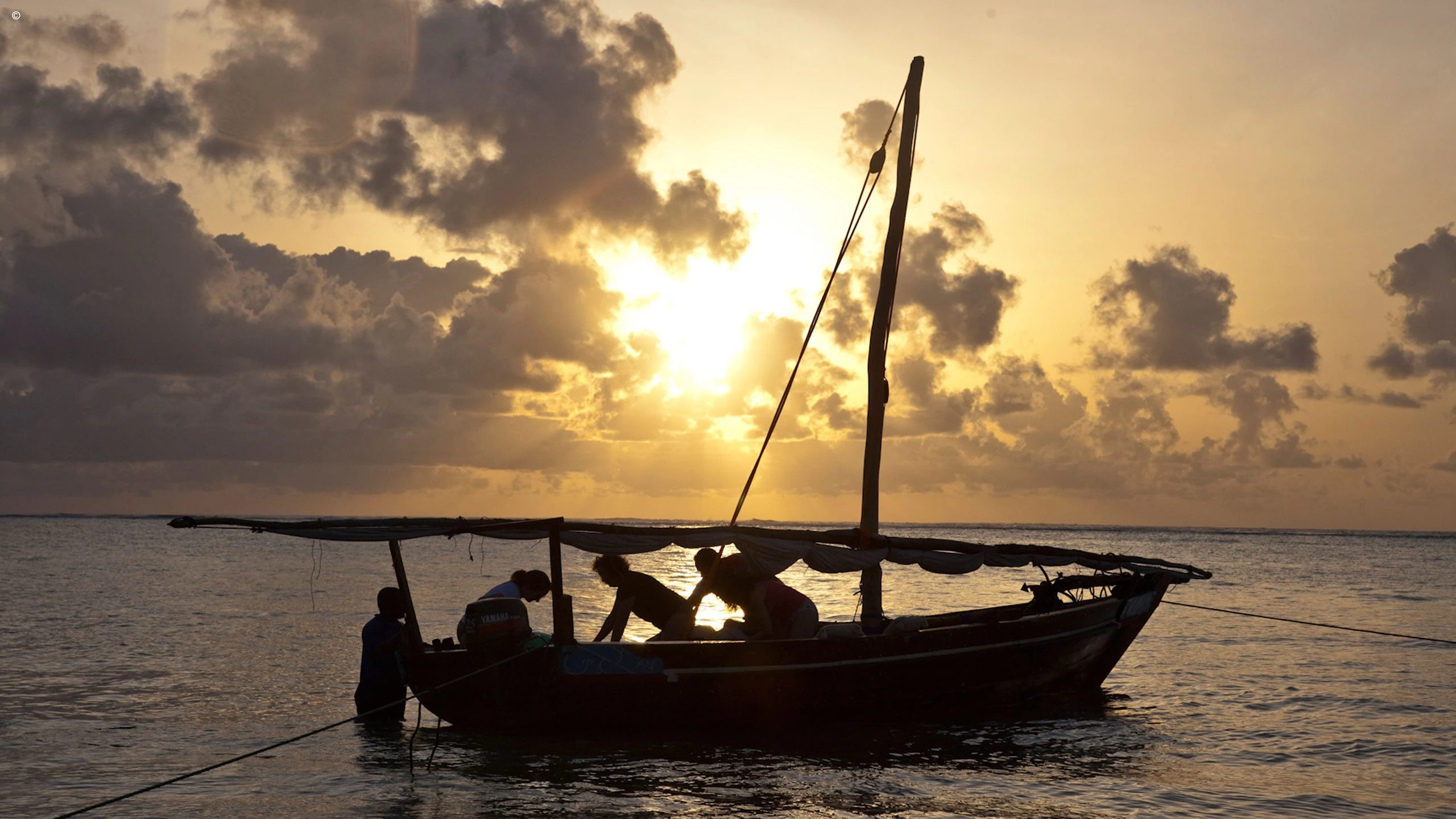 Dhow with fishermen silhouetted against a golden sunset