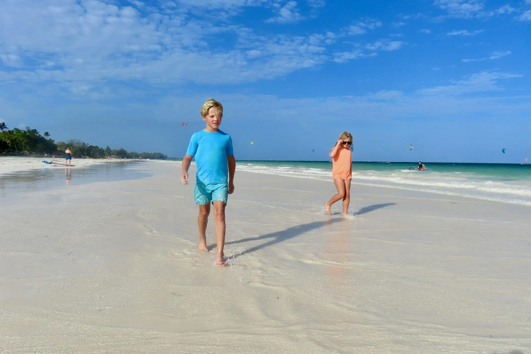 Two children walking on a pale beach under blue sky