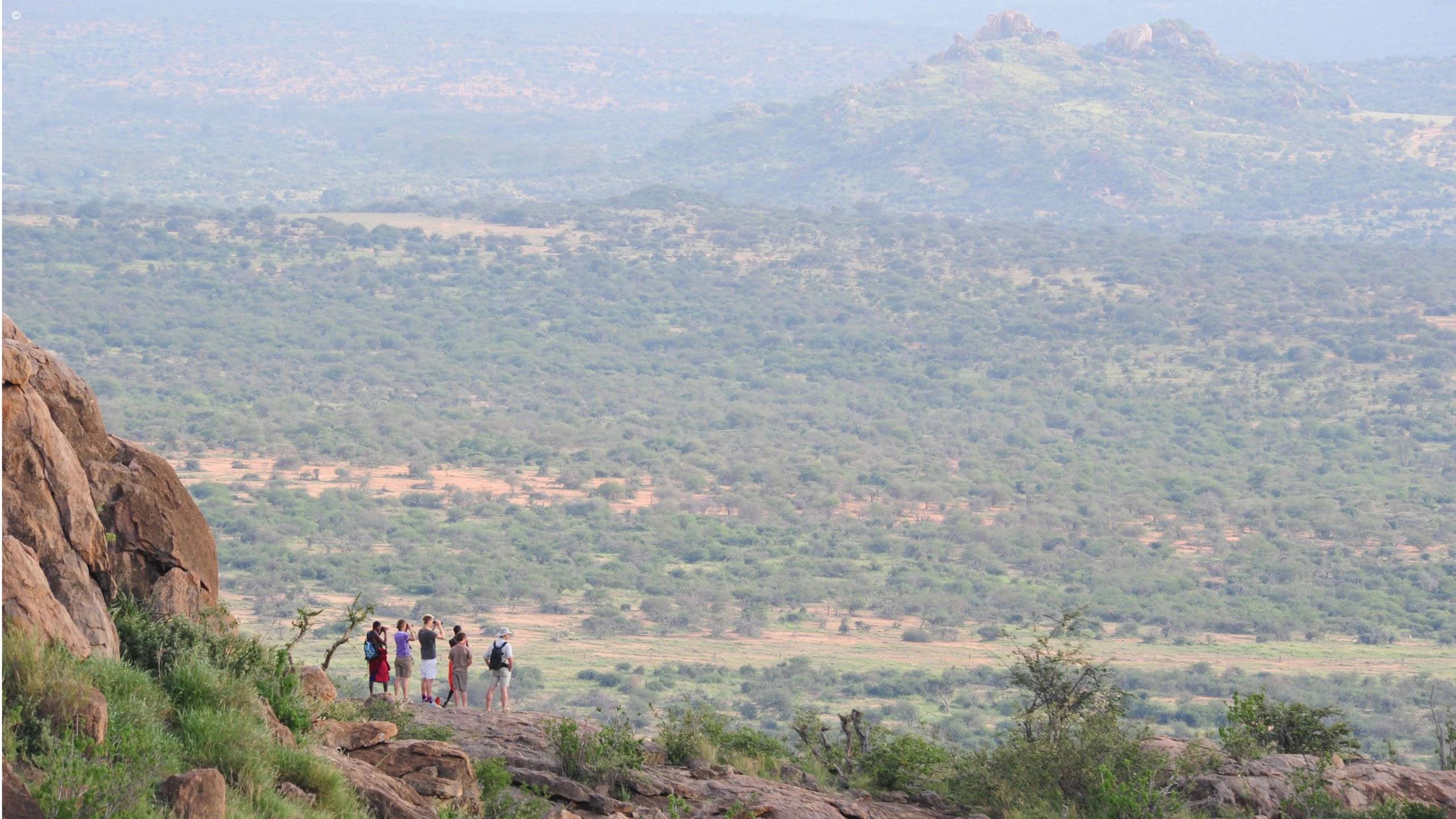 Hikers on a rocky viewpoint above wide wooded valleys