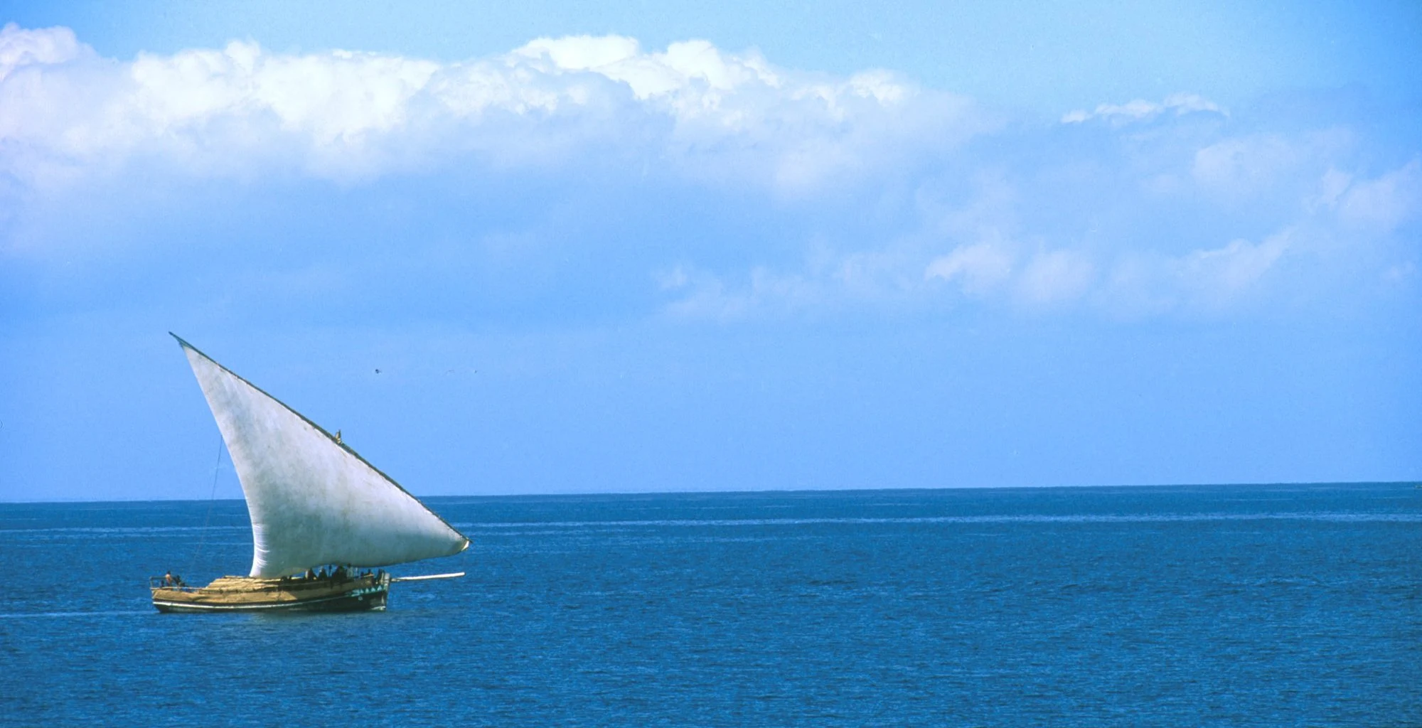 A traditional dhow sailing on a deep blue sea under light cloud