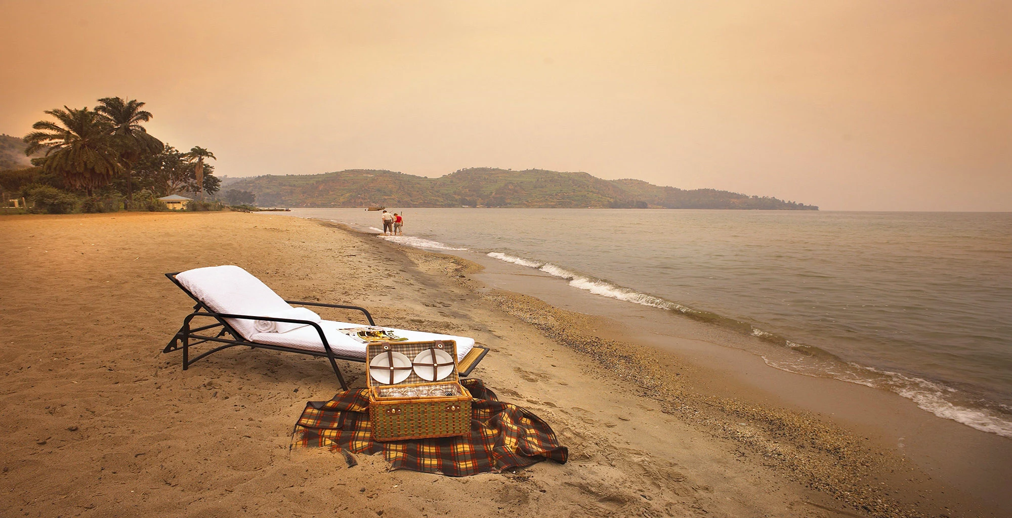 A sun lounger and picnic blanket on a sandy Lake Kivu beach at dusk